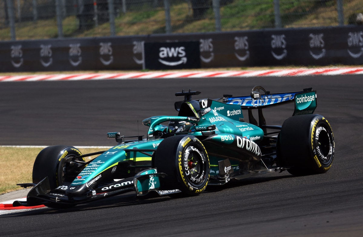 En turkos och svart Formel 1-bil kör på en racerbana med röd och vit kantmarkering. Bilen är fotograferad från sidan under körning.