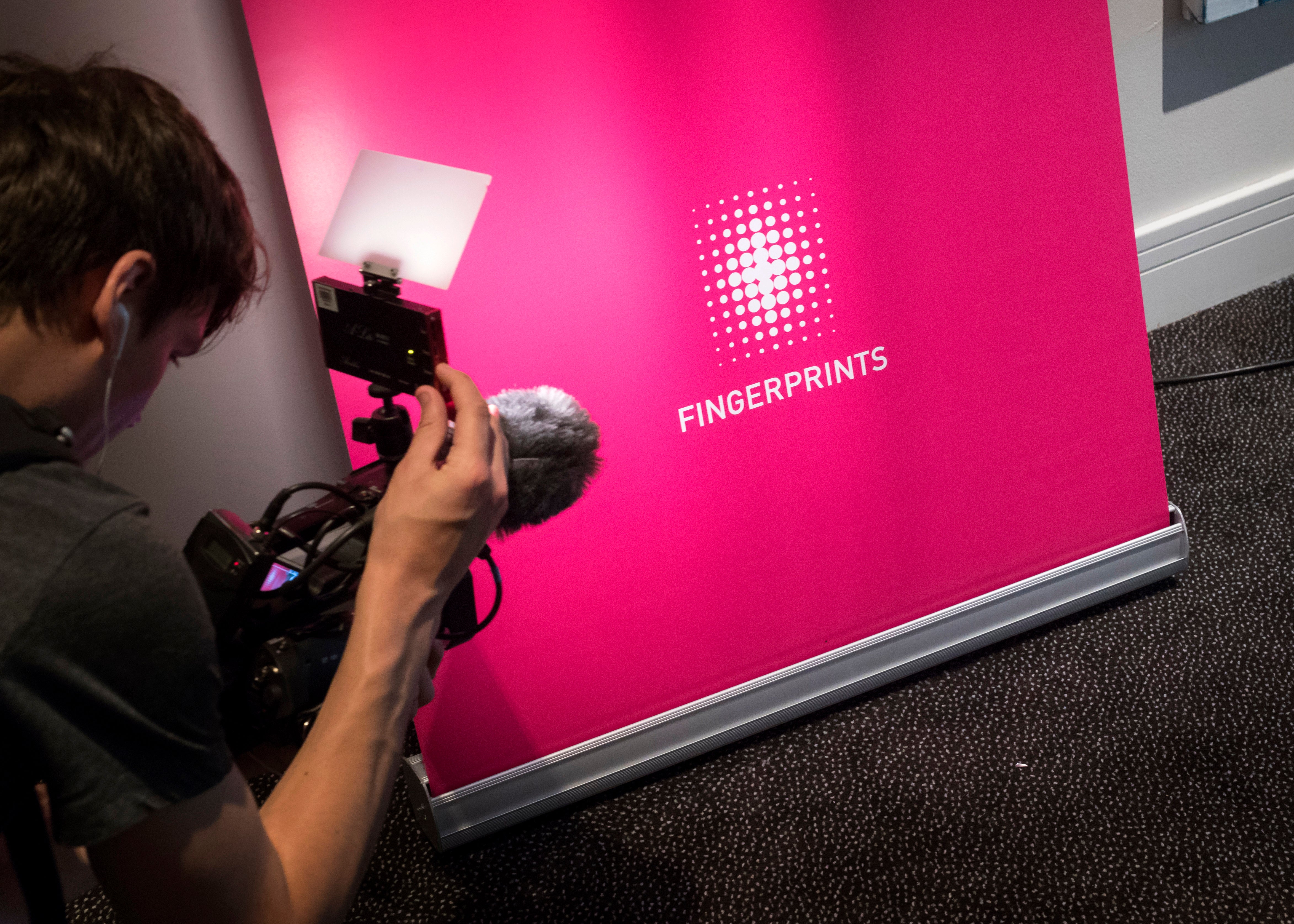 Person filmar en rosa vägg med Fingerprints-logotyp och text.