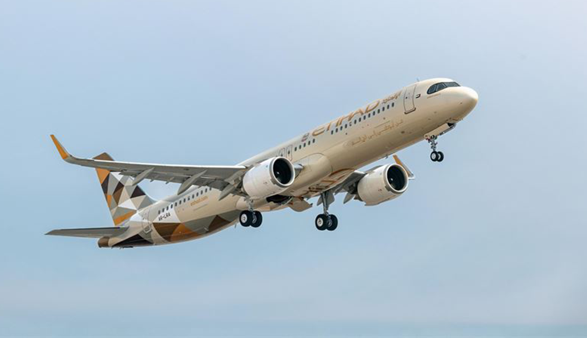 Ett Etihad Airways-flygplan i luften mot en klar blå himmel. Planet har vit och guldbrunt färgschema.