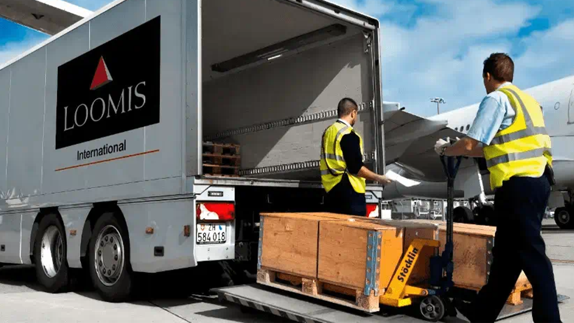 Arbetare i gula västar lastar paket på en Loomis-lastbil på en logistikanläggning.