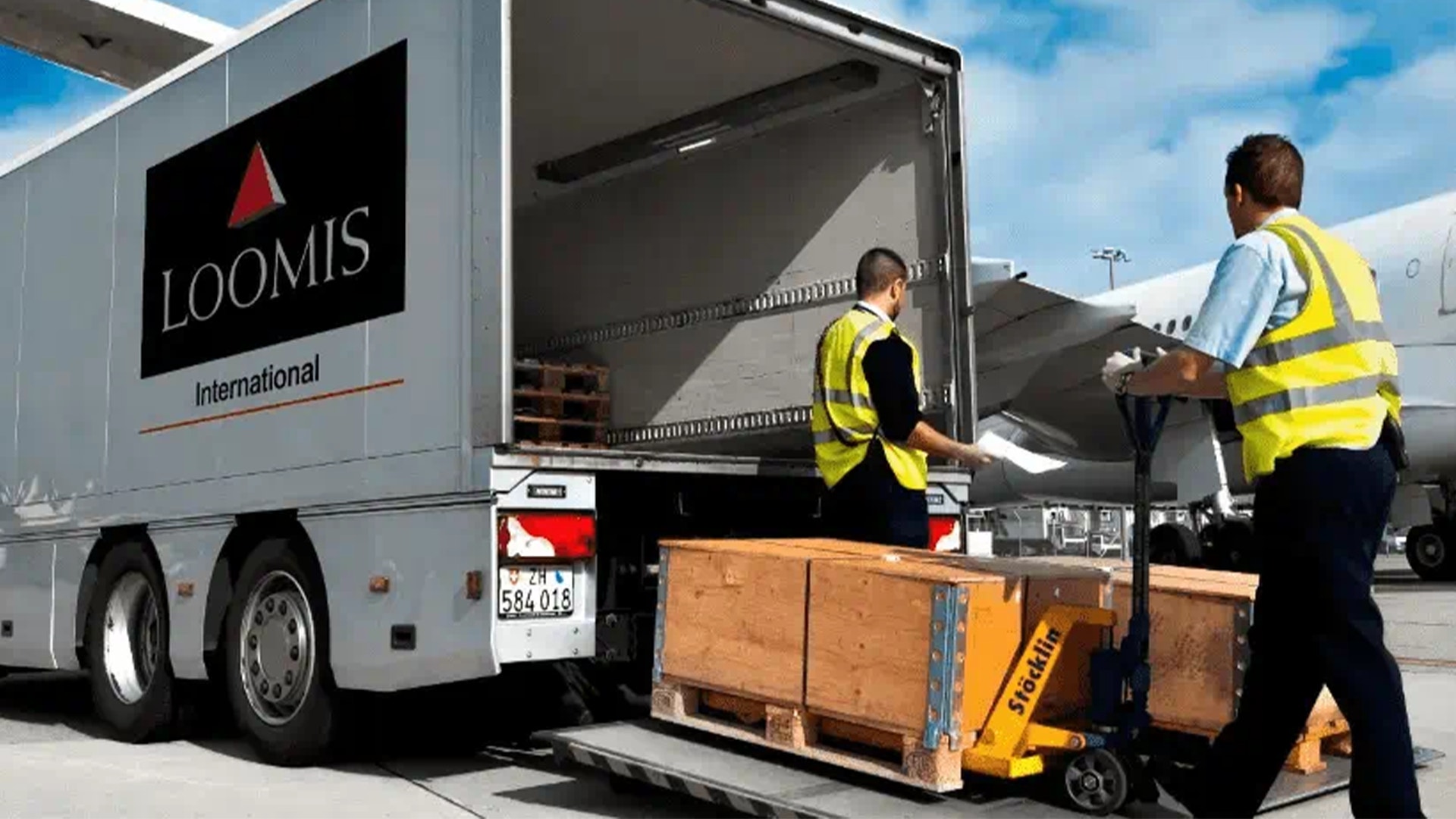 Arbetare i gula västar lastar paket på en Loomis-lastbil på en logistikanläggning.