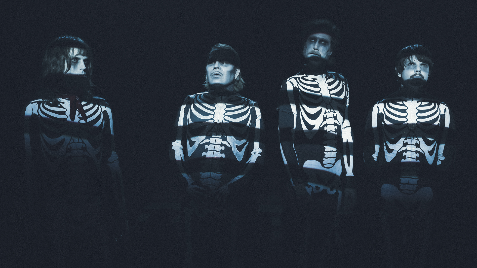 Fyra personer i skelettdräkter mot mörk bakgrund