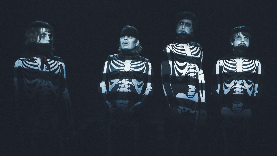 Fyra personer i skelettdräkter mot mörk bakgrund