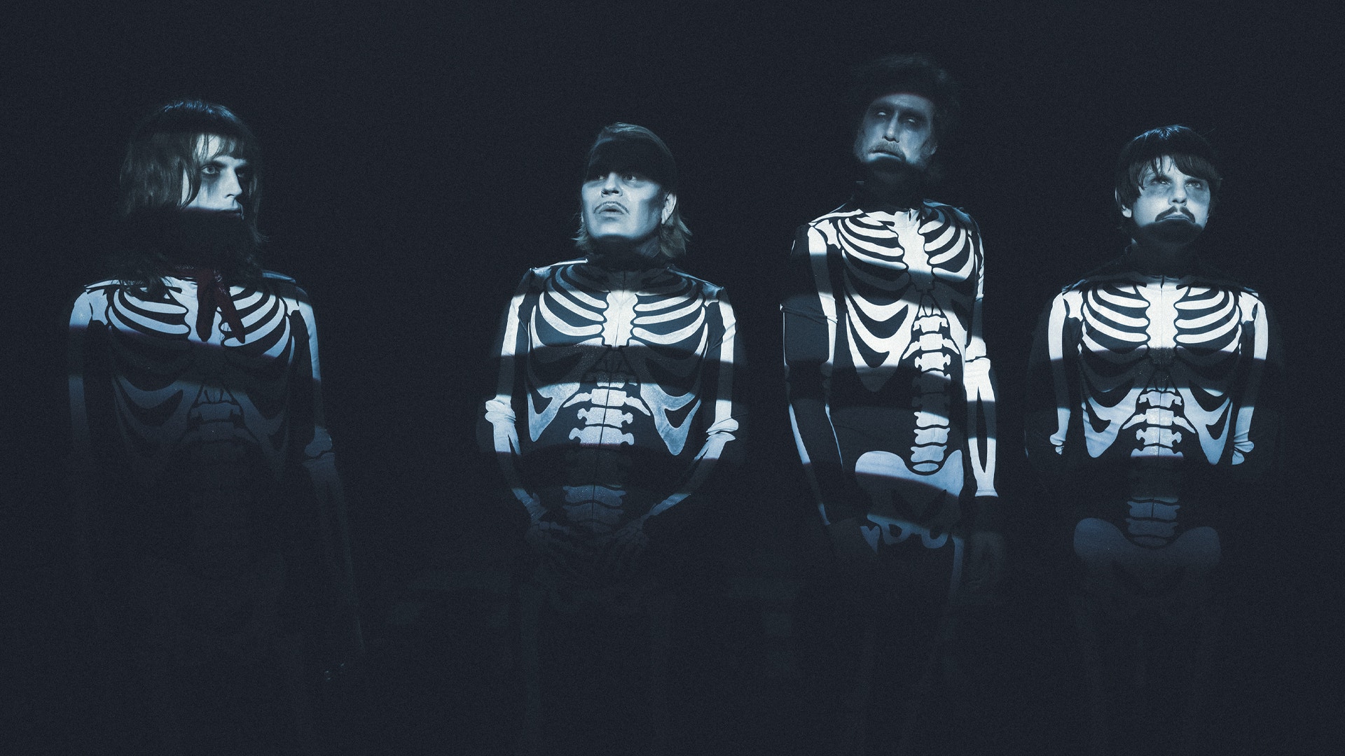 Fyra personer i skelettdräkter mot mörk bakgrund