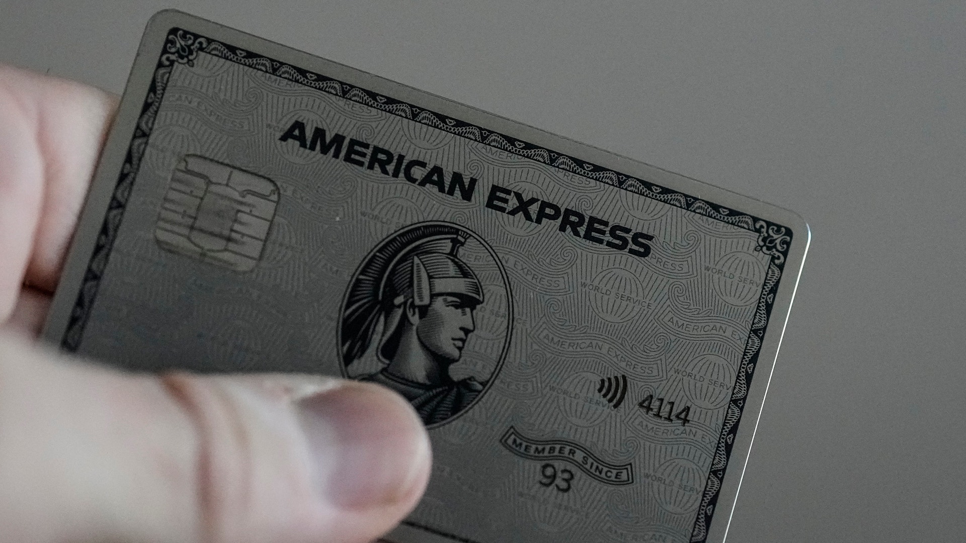 En hand som håller ett grått American Express-kort med metallfinish och det klassiska American Express-logotypen synlig.
