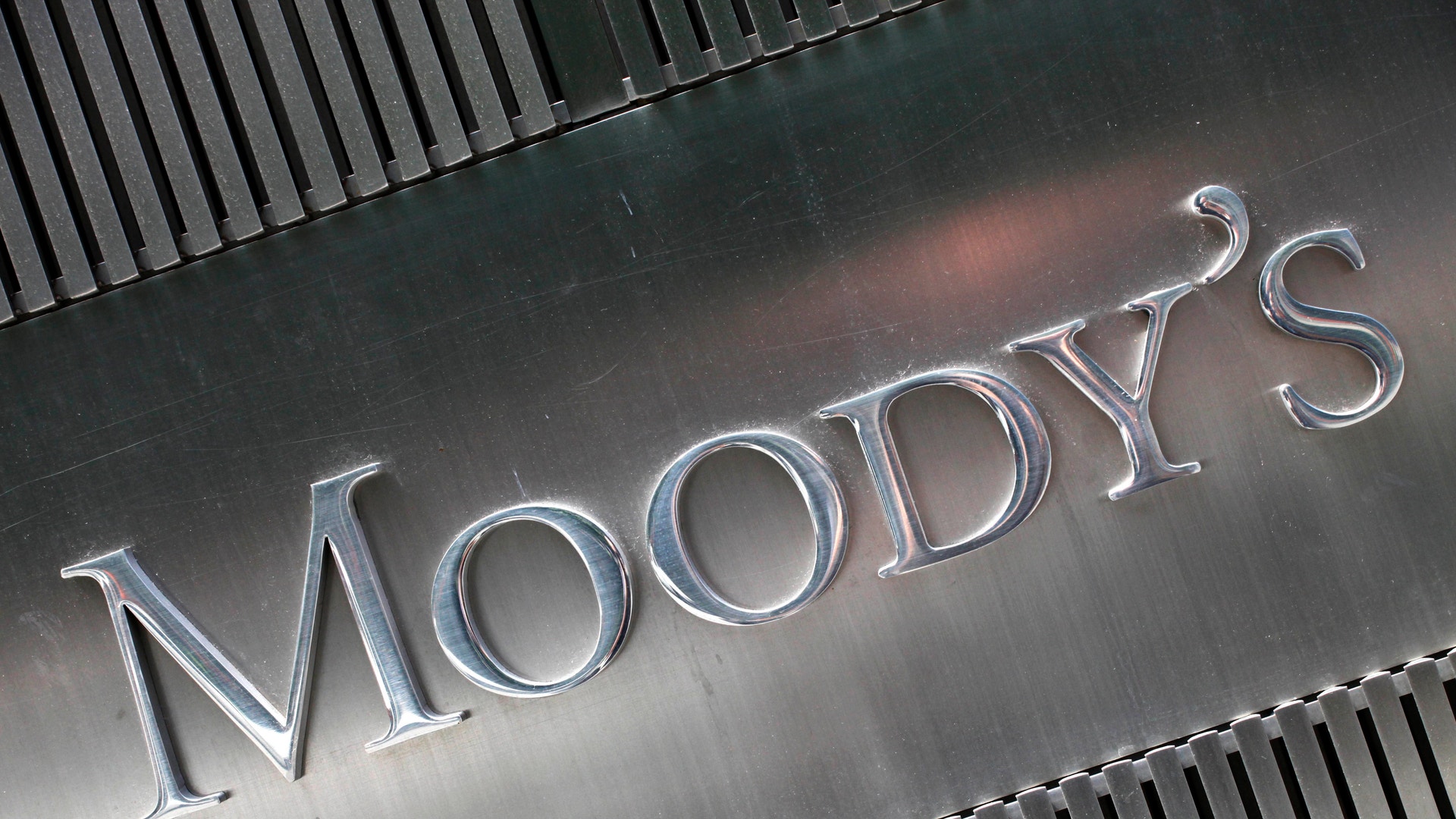 Metallisk skylt med texten Moody's präglad i silverfärgad metall, omgiven av vertikala metallribbor.