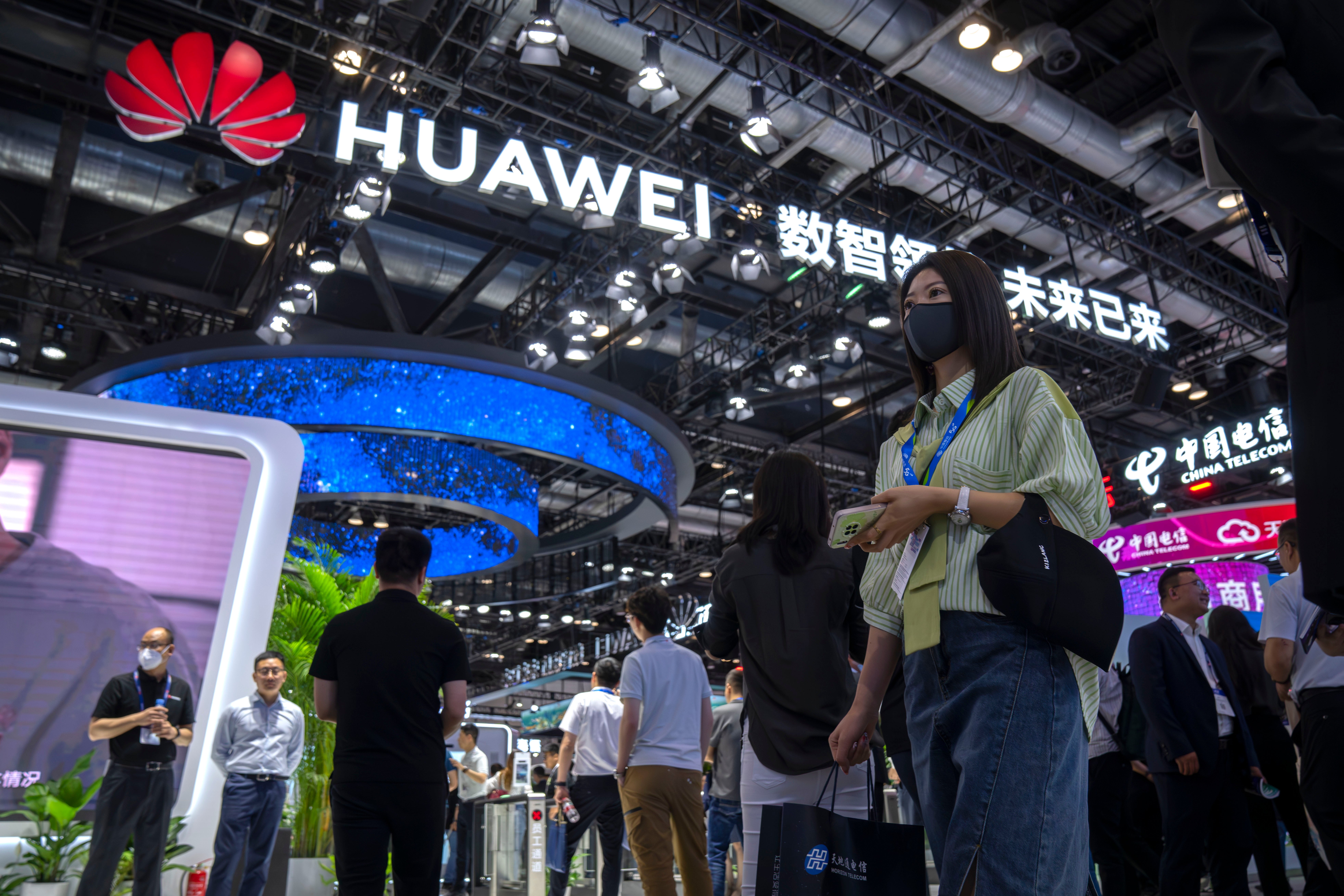 Besökare med munskydd går förbi en monter från det kinesiska teknikföretaget Huawei på PT Expo i Peking.