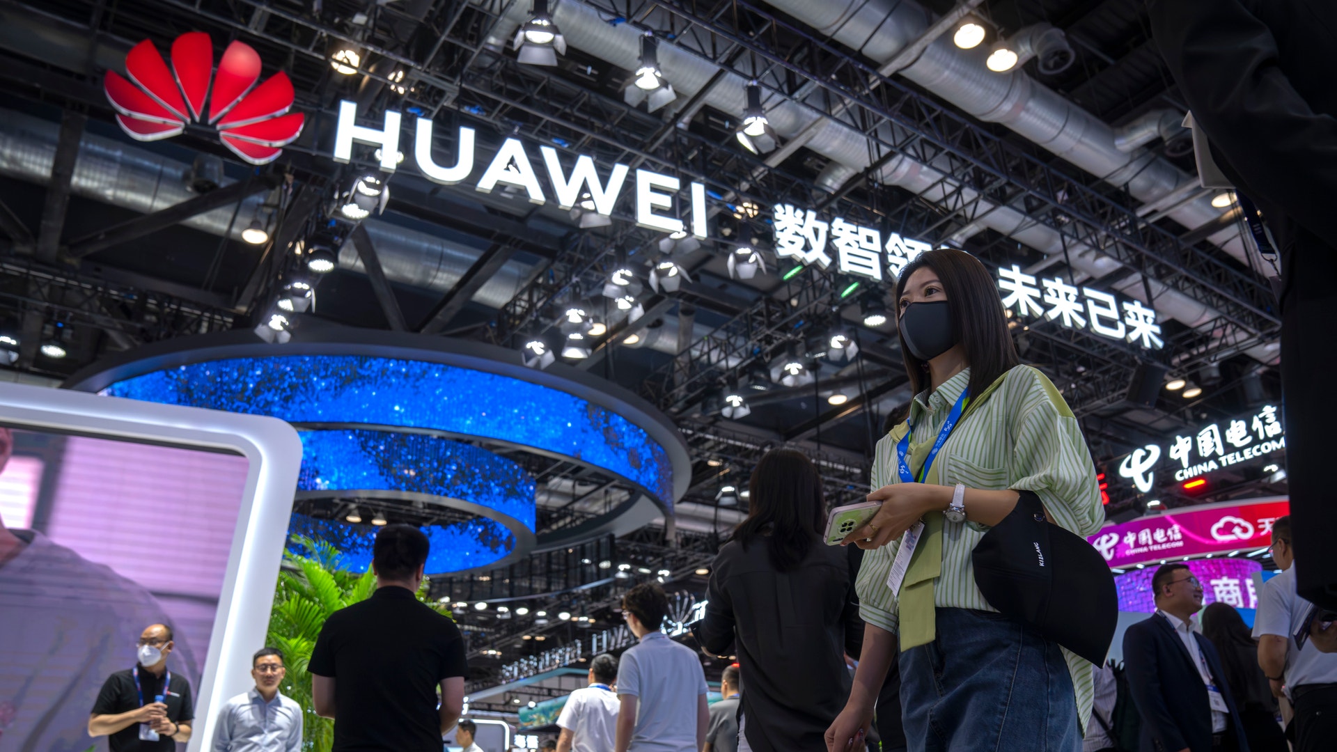 Besökare med munskydd går förbi en monter från det kinesiska teknikföretaget Huawei på PT Expo i Peking.