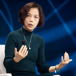 En kvinna som presenterar på en scen framför en blå bakgrund.