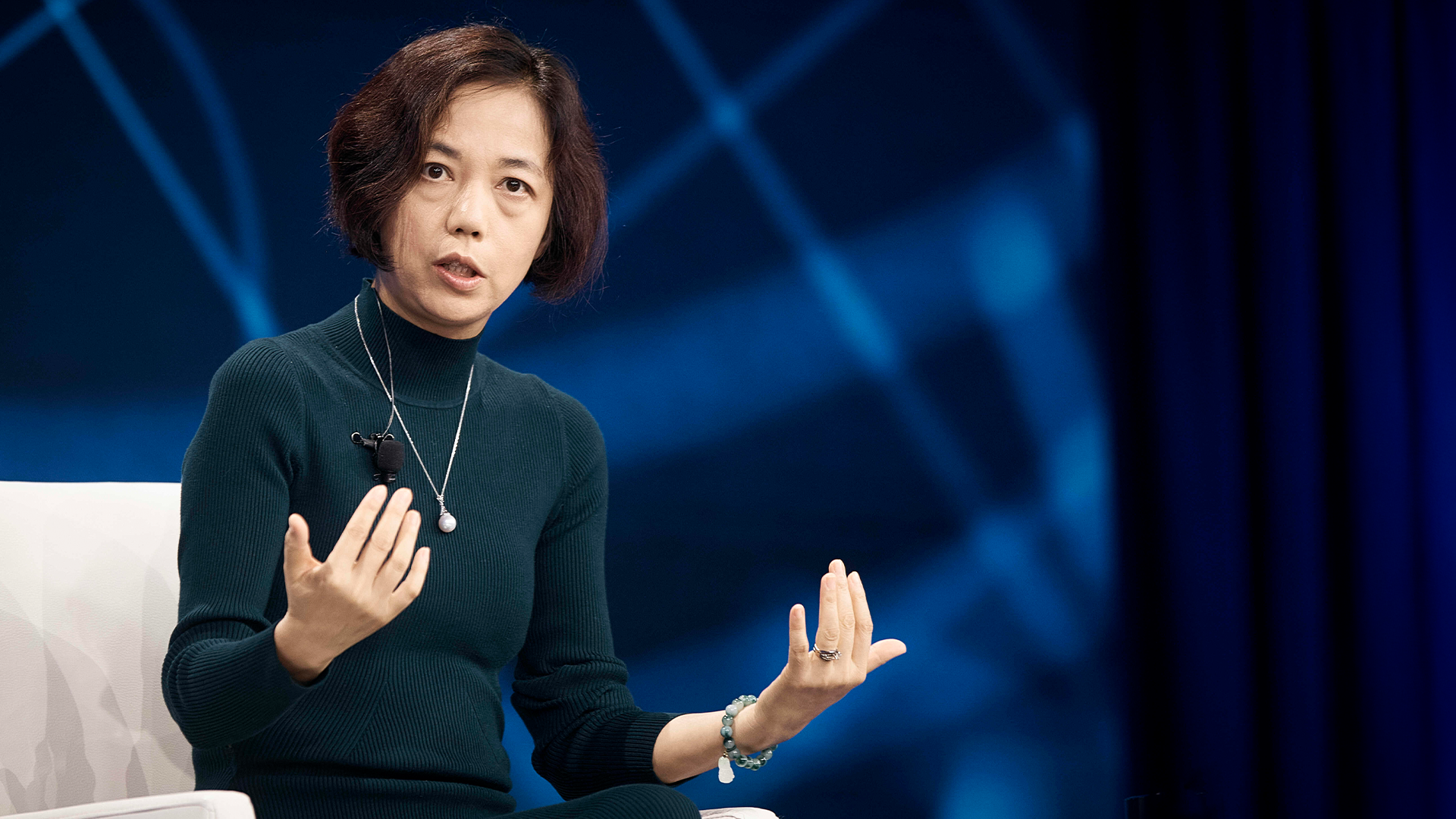 En kvinna som presenterar på en scen framför en blå bakgrund.