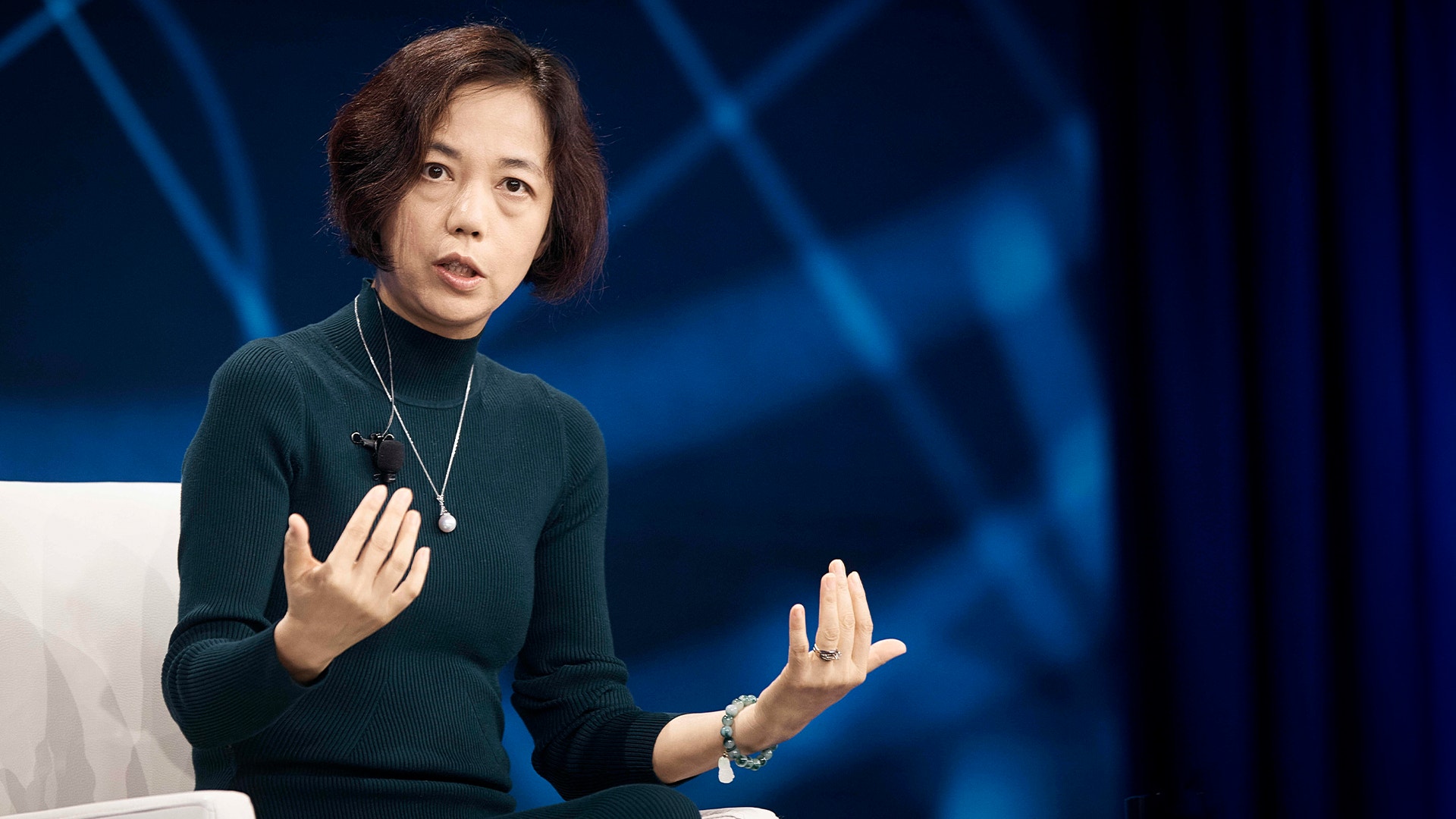 En kvinna som presenterar på en scen framför en blå bakgrund.