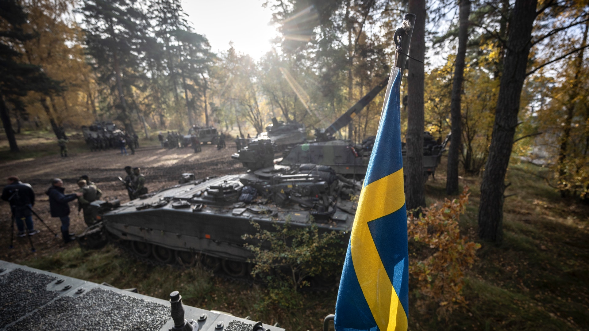 Svensk flagga på försvarsutrustning som står i skogen tillsammans med flera soldater.