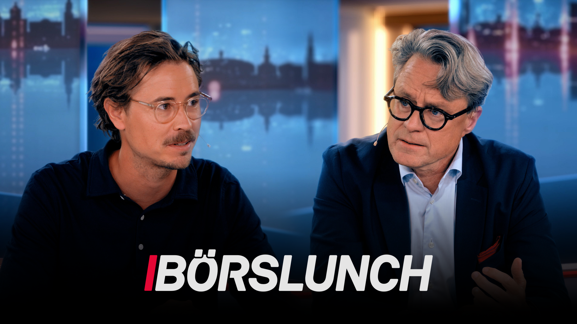 Två män sitter vid ett bord i en TV-studio. I bakgrunden syns en stadshorisont. Texten Börslunch visas längst ner på skärmen.