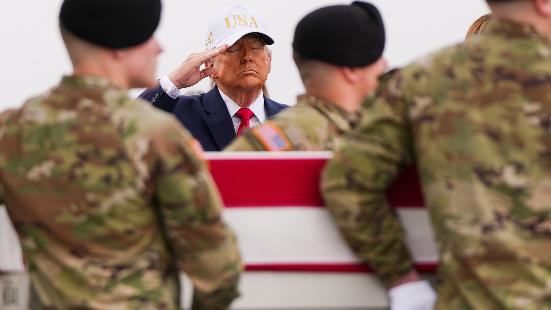 En person i formell klädsel och USA-keps saluterar framför militär personal i kamouflagekläder.