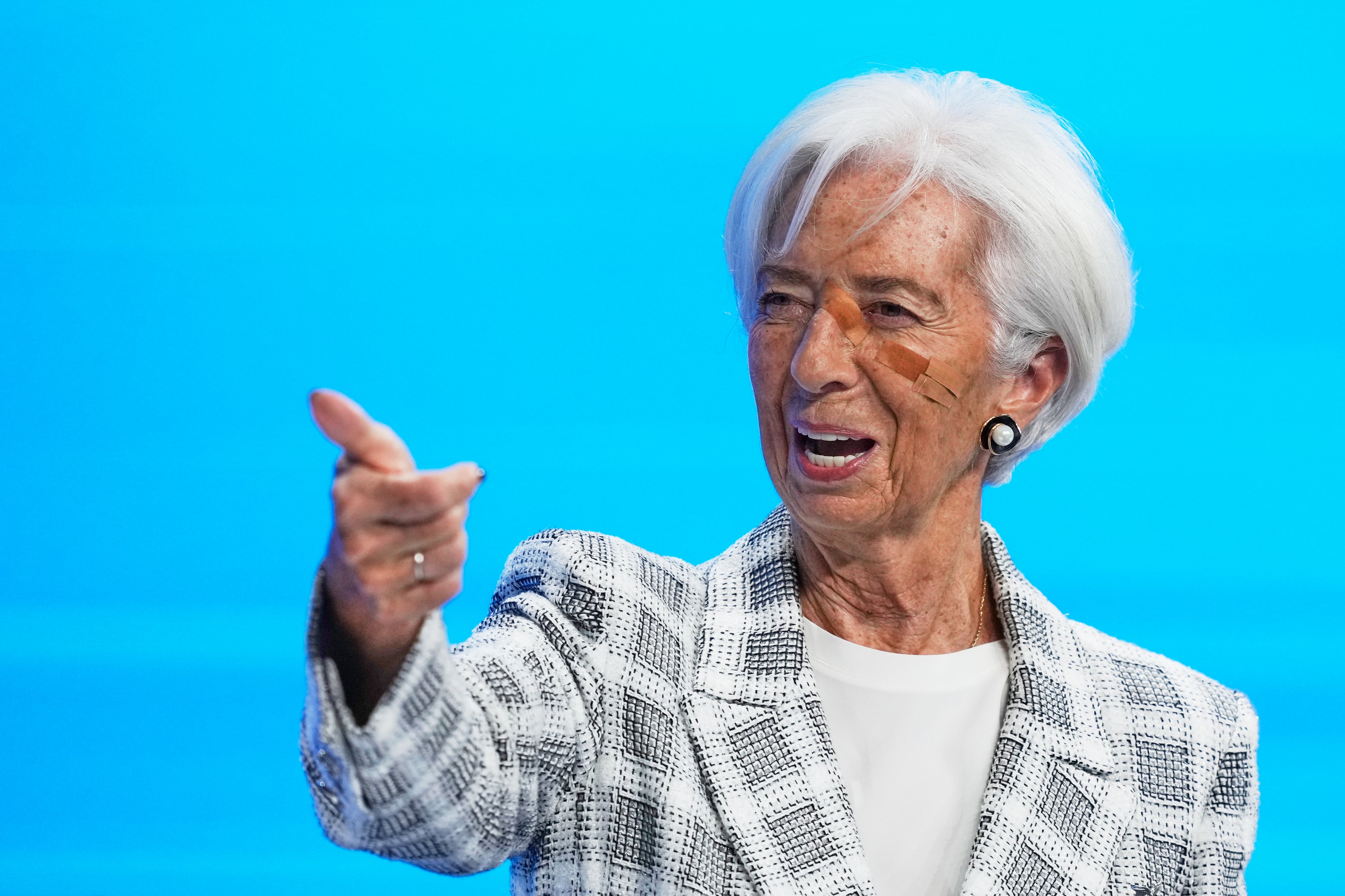 Christine Lagarde med kort vitt hår och rutig kavaj pekar framåt med handen och talar mot en klarblå bakgrund.