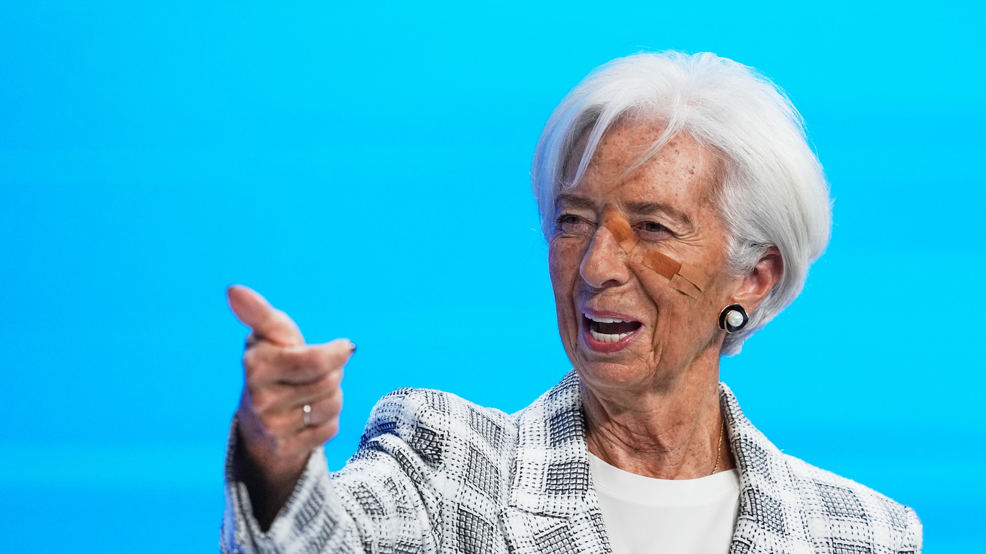 Christine Lagarde med kort vitt hår och rutig kavaj pekar framåt med handen och talar mot en klarblå bakgrund.