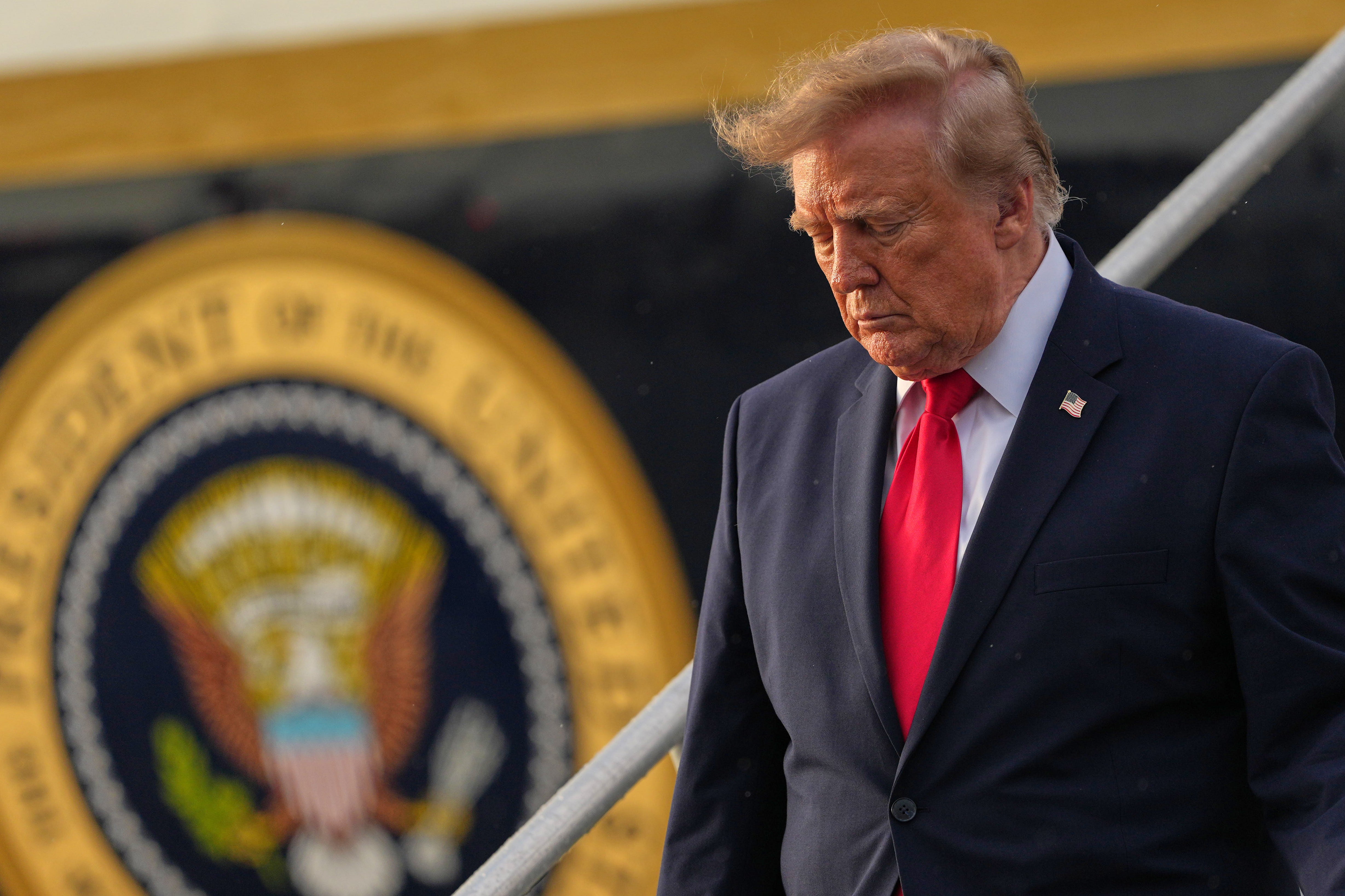 En äldre man i mörk kostym och röd slips går nedför en trappa med blicken riktad nedåt. Bakom honom syns USA:s presidentsigill.