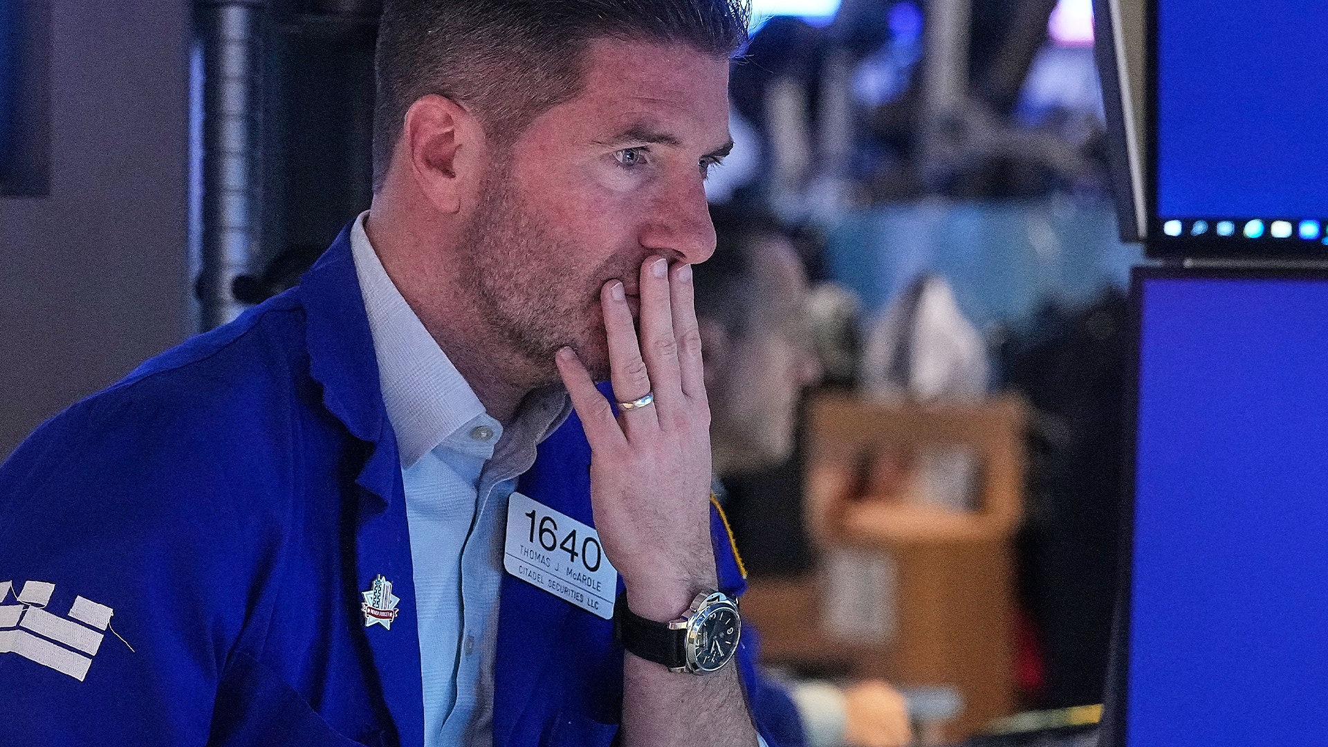 Man i blå jacka med badge ser tankfull ut med handen mot ansiktet