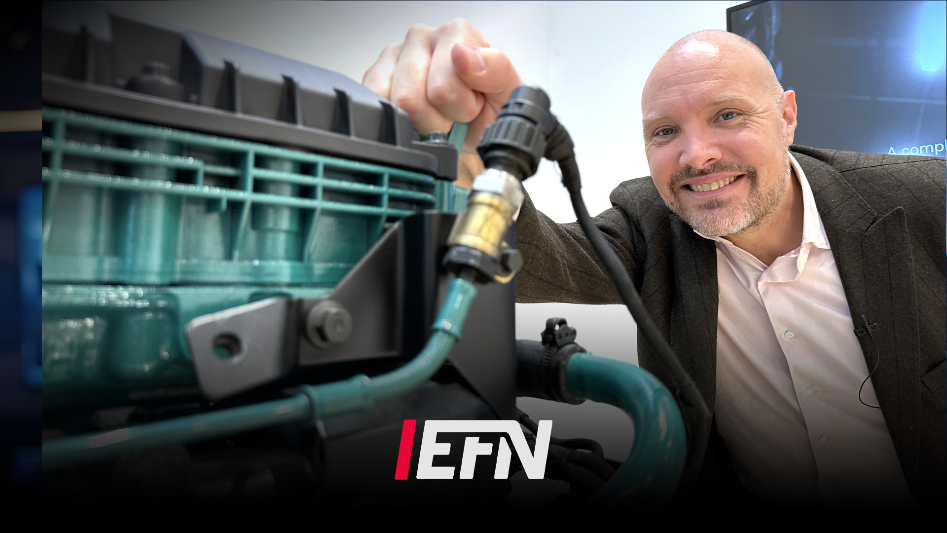En man i kostym presenterar en bilkomponent framför en bilmotor. EFN-logga visas i bilden.