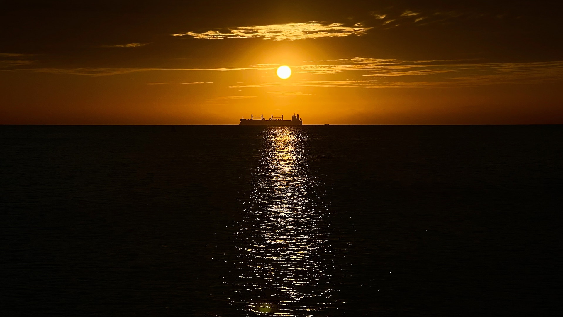 Solnedgång över havet med ett oljetankfartyg i siluett mot den gula solen.
