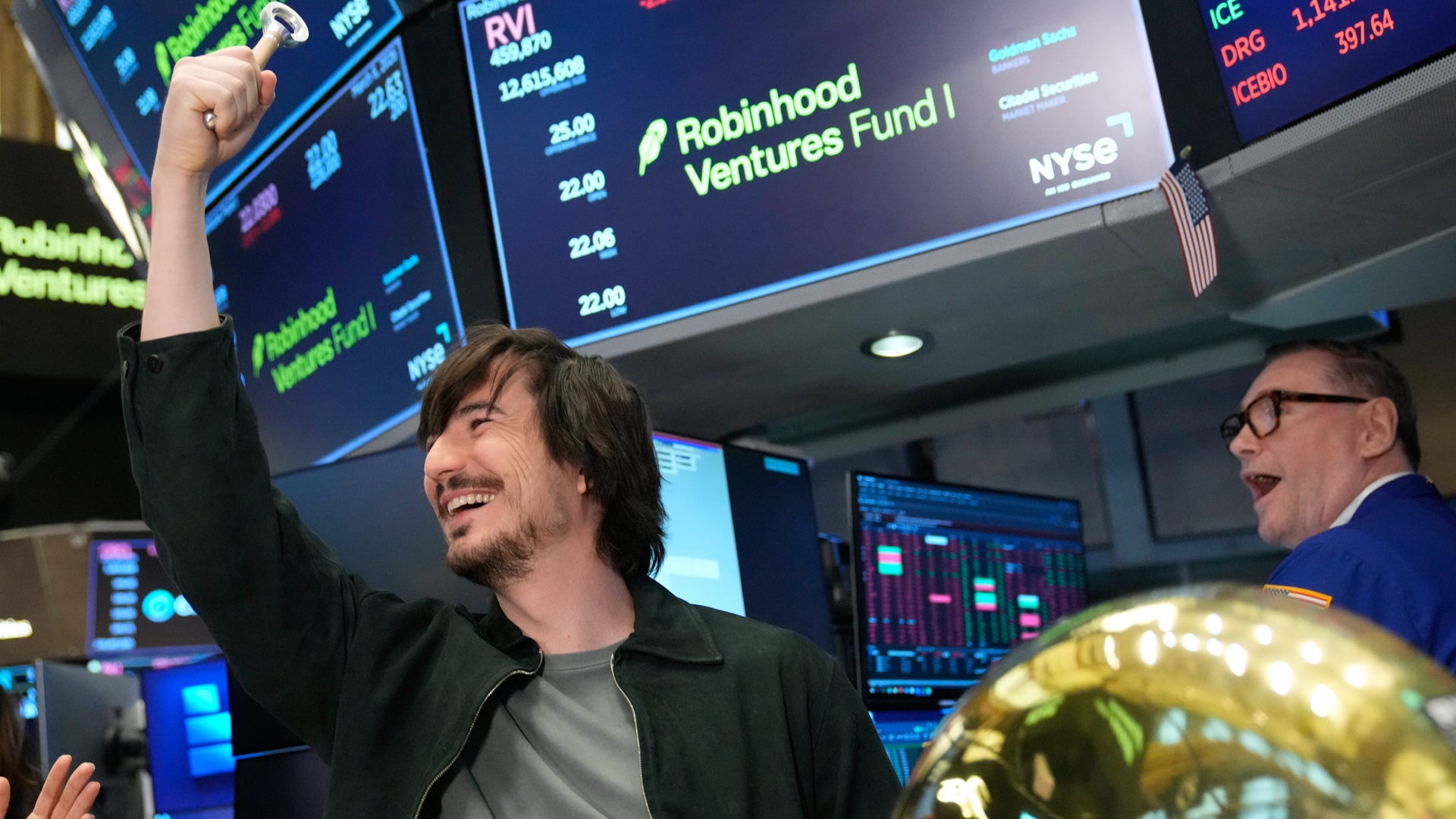 Två män firar på en börs med digitala marknadsvisningar i bakgrunden.