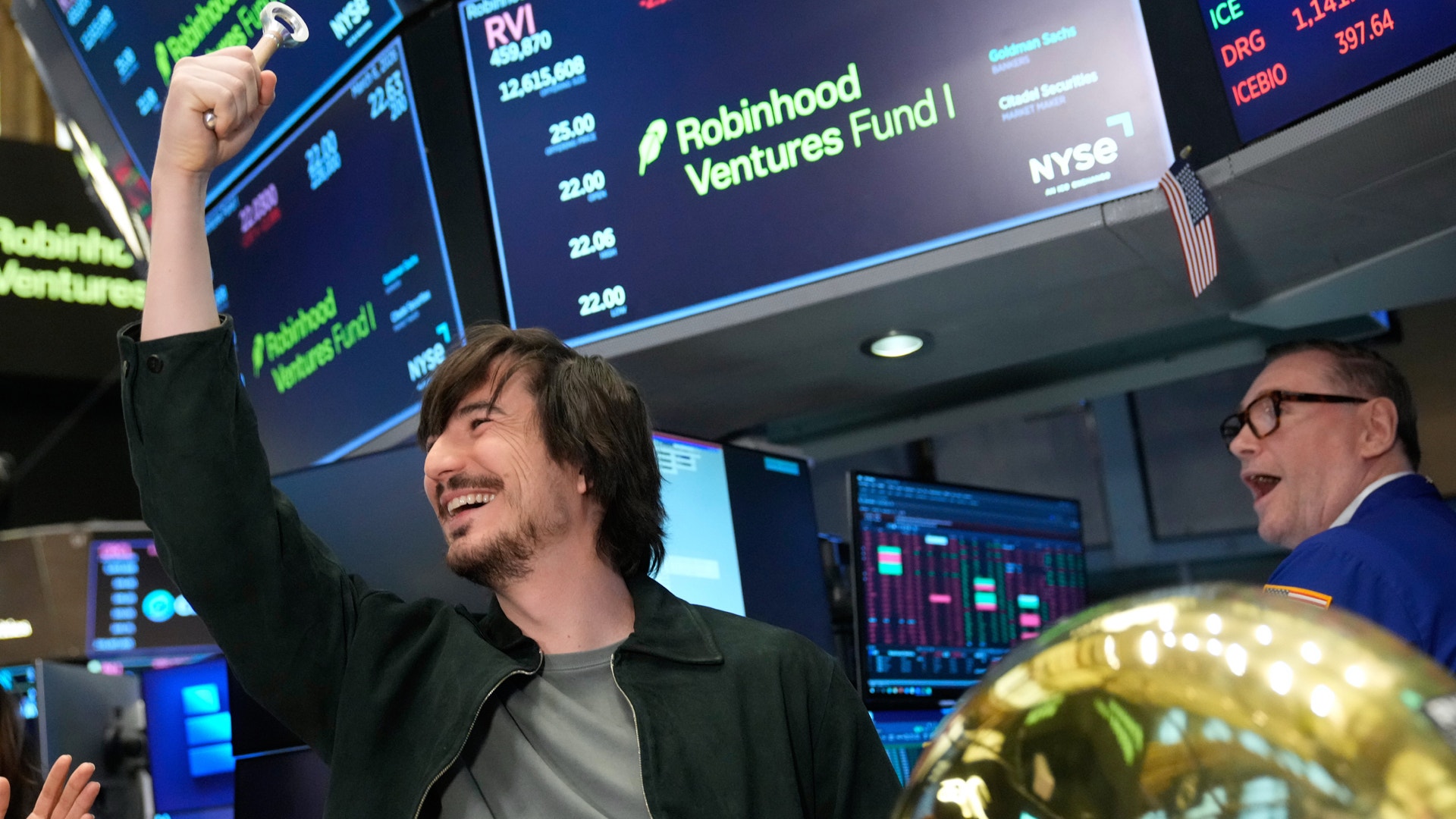 Två män firar på en börs med digitala marknadsvisningar i bakgrunden.