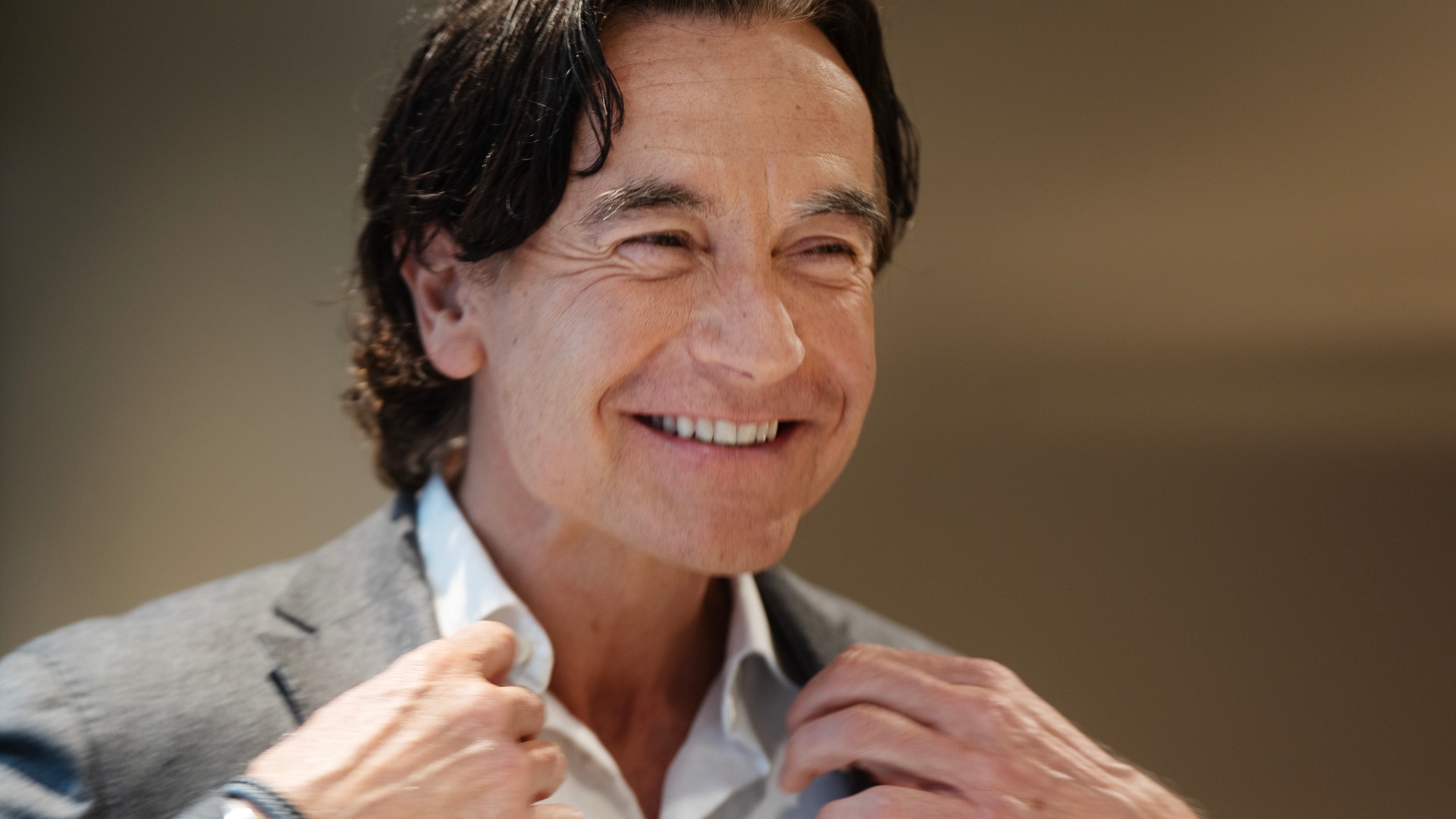 Porträtt av en man som ler mot kameran, iklädd grå kavaj och vit skjorta.