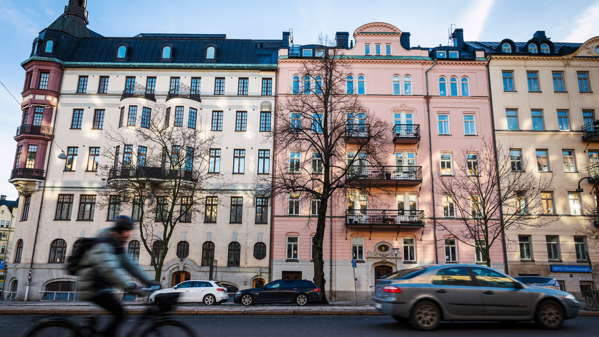 Rad av klassiska flervåningshus med färgade fasader längs en stadsgata med bilar och fotgängare