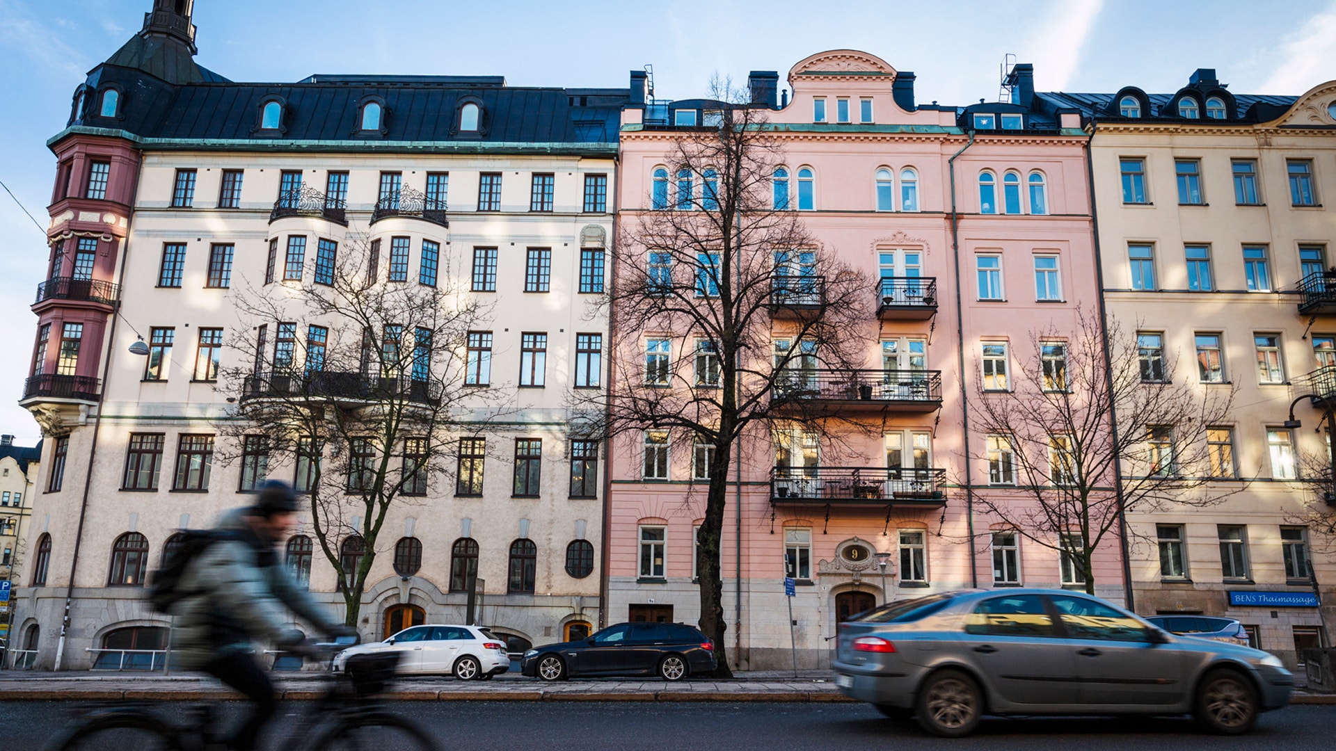 Rad av klassiska flervåningshus med färgade fasader längs en stadsgata med bilar och fotgängare