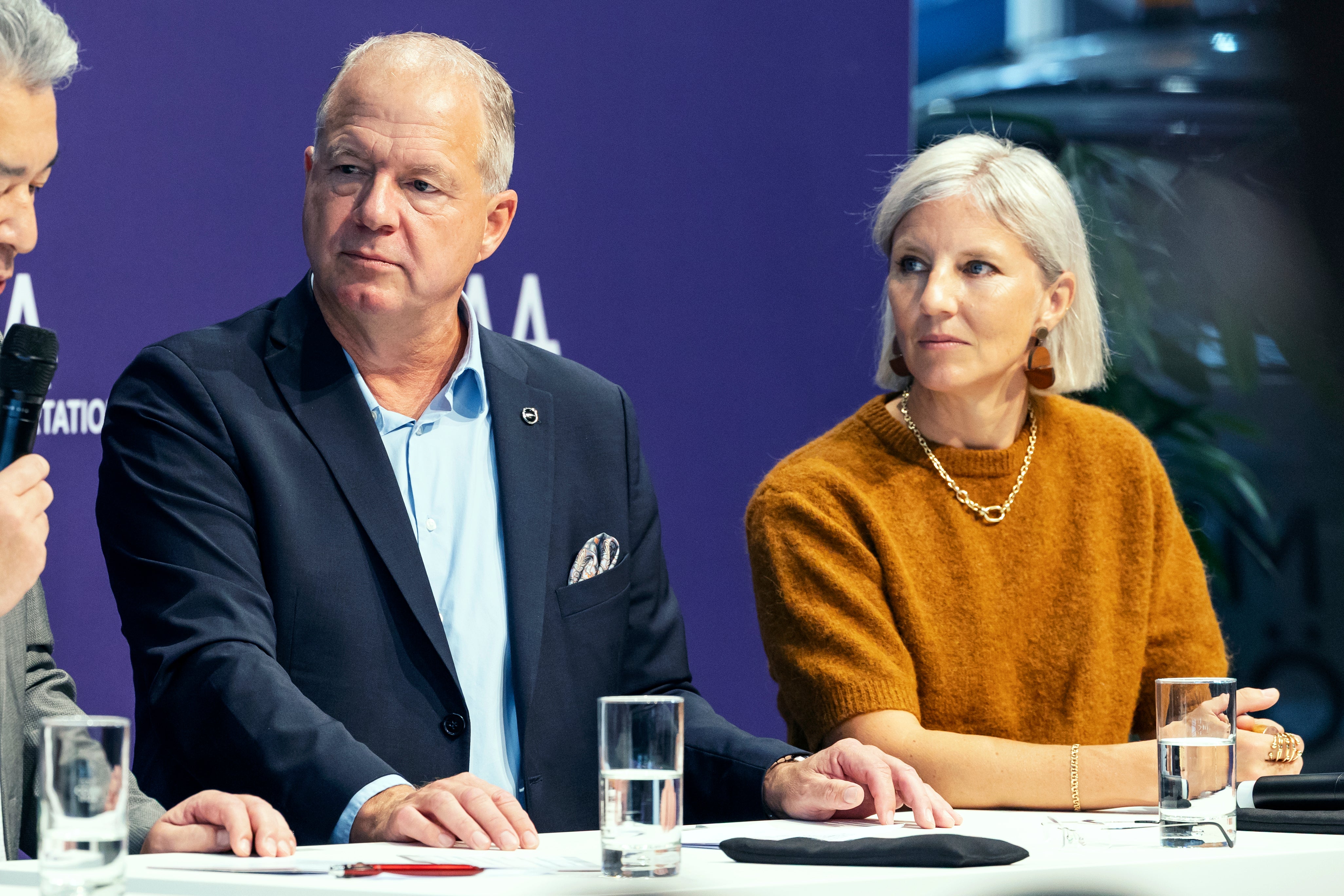En man och en kvinna sitter bredvid varandra vid ett bord under en pressträff eller paneldiskussion.