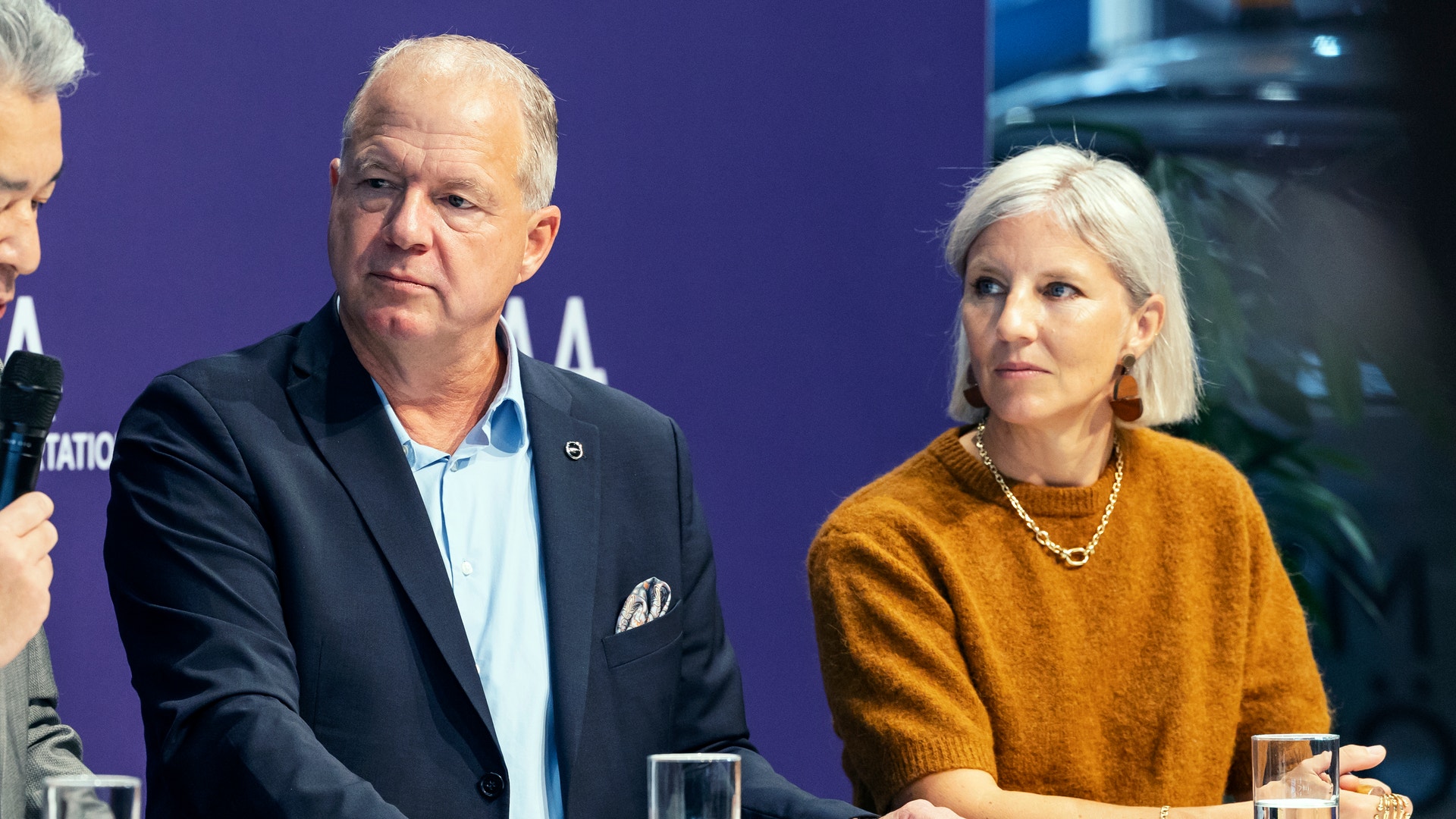En man och en kvinna sitter bredvid varandra vid ett bord under en pressträff eller paneldiskussion.