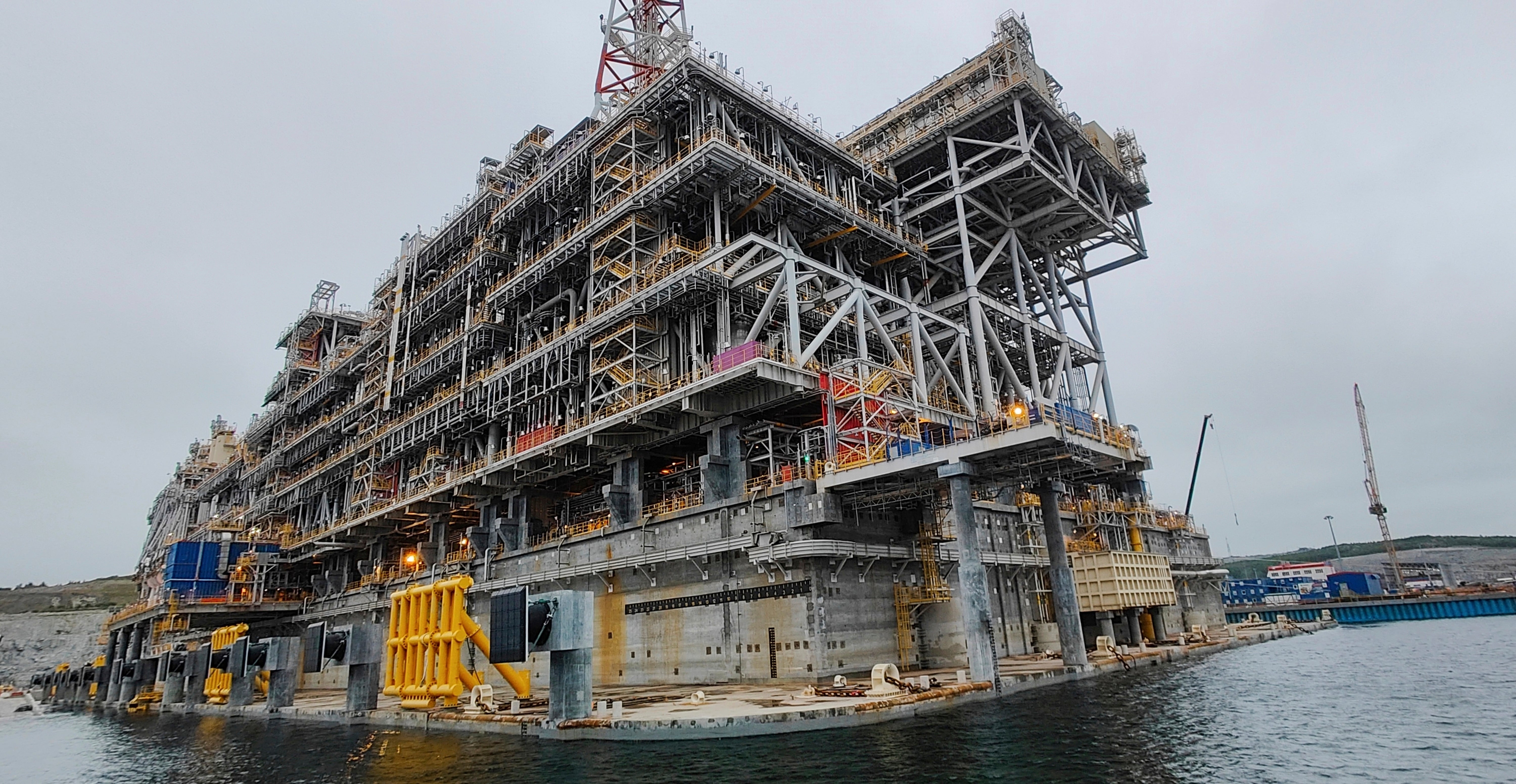Stor industriell plattform av stål vid en kaj, sedd från vattnet under mulen himmel.