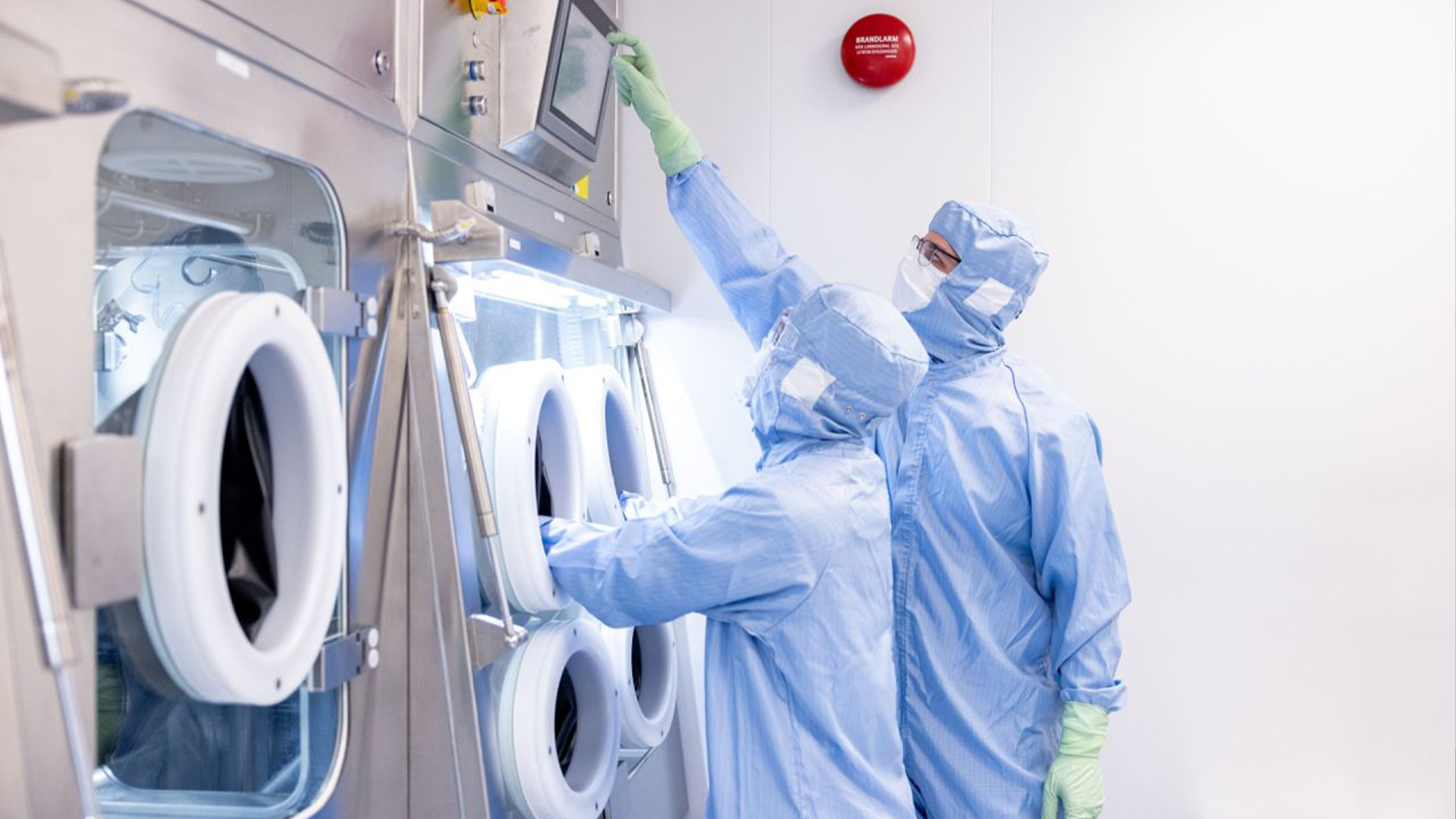 Två personer i skyddskläder arbetar i ett laboratorium med renrumsutrustning.