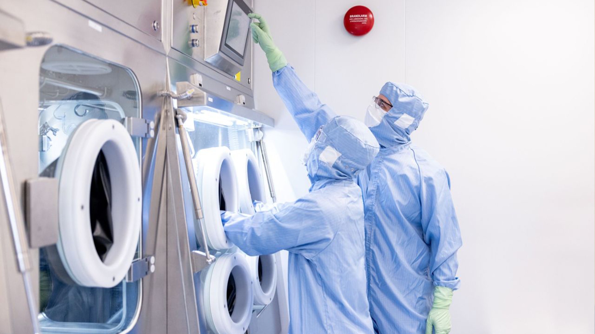 Två personer i skyddskläder arbetar i ett laboratorium med renrumsutrustning.