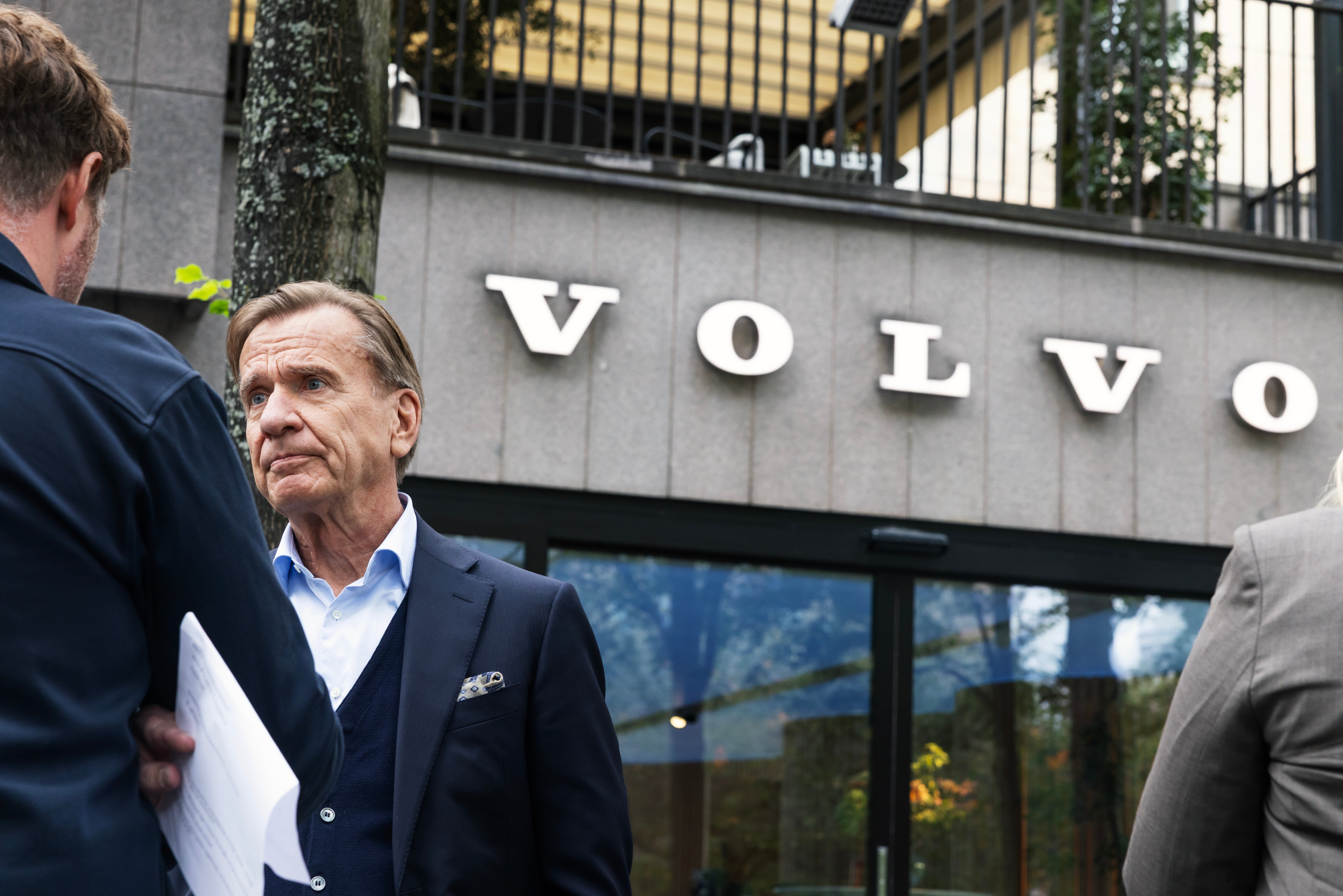 Håkan Samuelsson, vd för Volvo Cars, står utomhus framför en byggnad med Volvos logotyp och tittar allvarligt åt sidan.