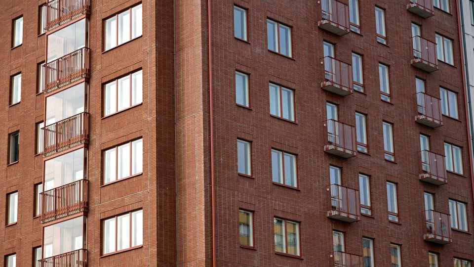 Bild på exteriören av ett nyproducerat lägenhetshus i tegel, med fönster och balkonger.