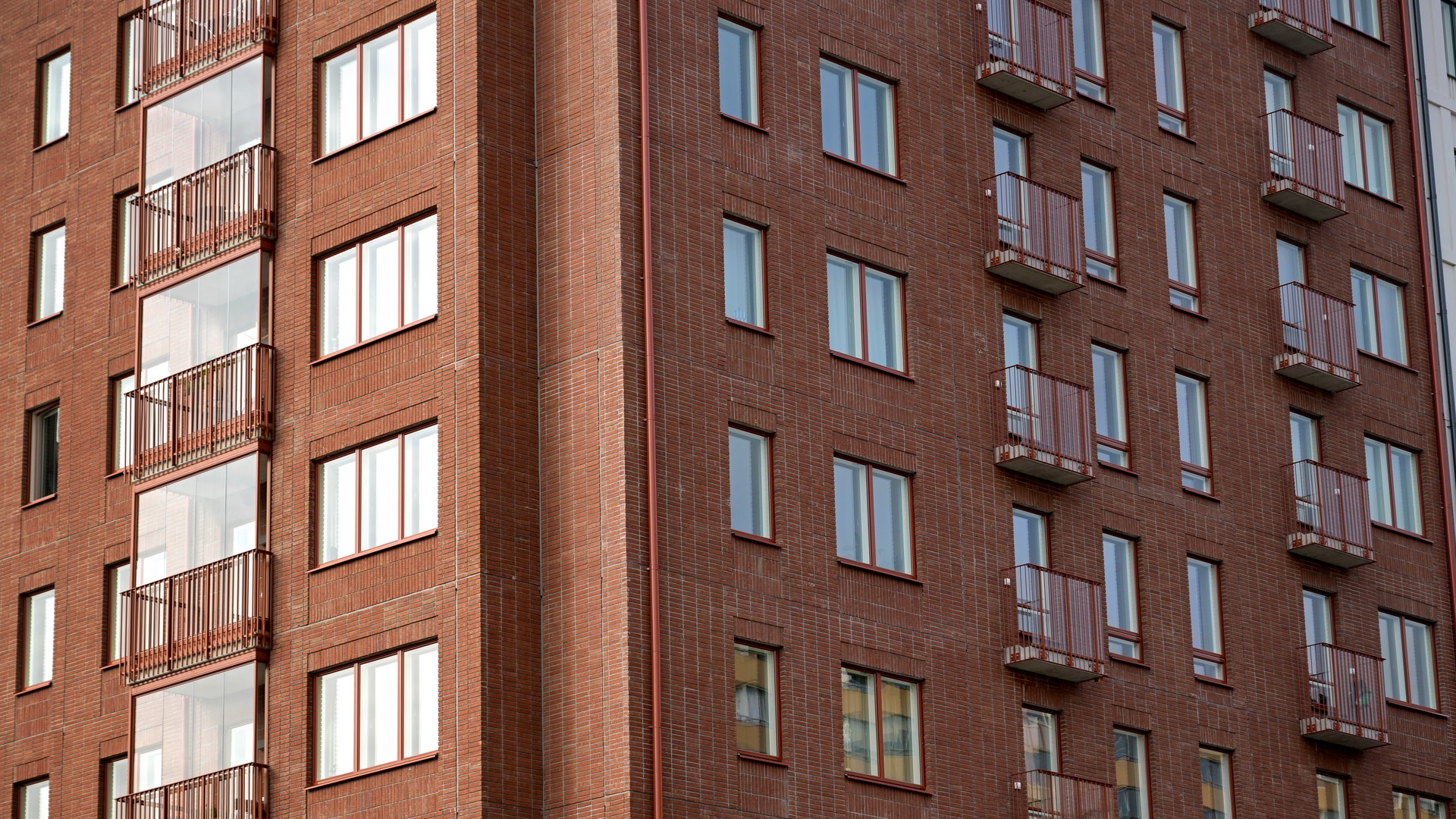 Bild på exteriören av ett nyproducerat lägenhetshus i tegel, med fönster och balkonger.