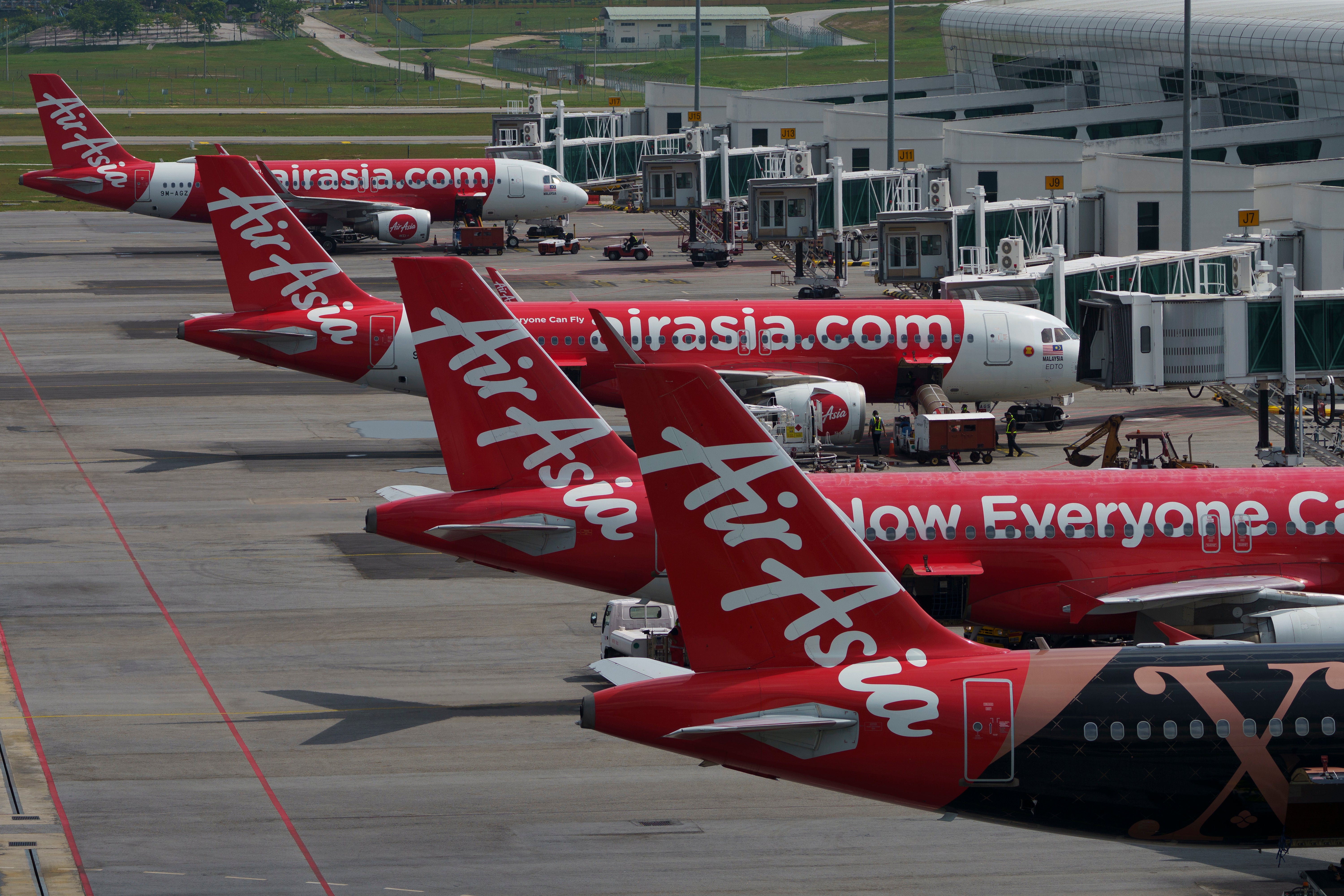 Flera röda AirAsia-flygplan parkerade vid gater på en flygplats.