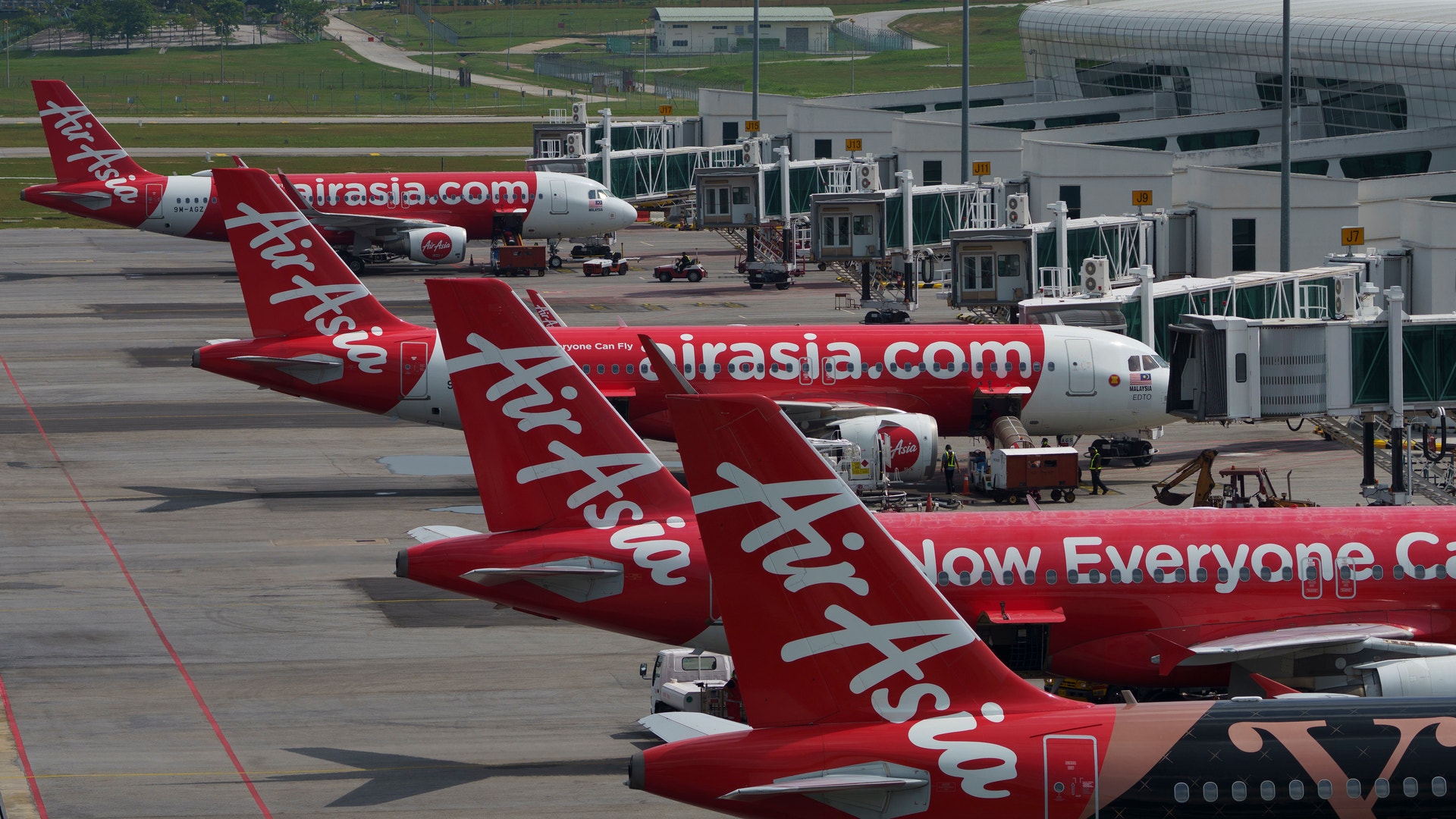 Flera röda AirAsia-flygplan parkerade vid gater på en flygplats.