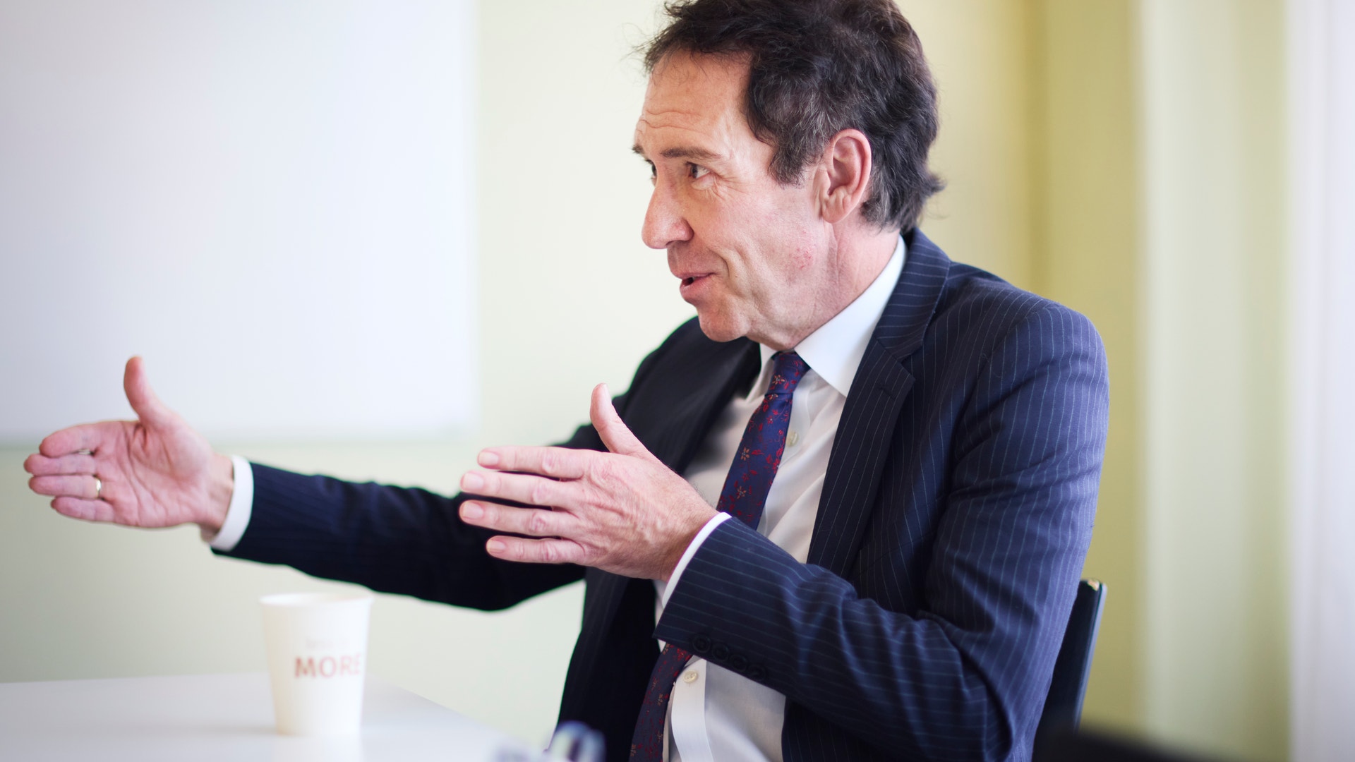 Byron Sharp är fotograferad i profil, sittandes vid ett bord och gestikulerandes med händerna.