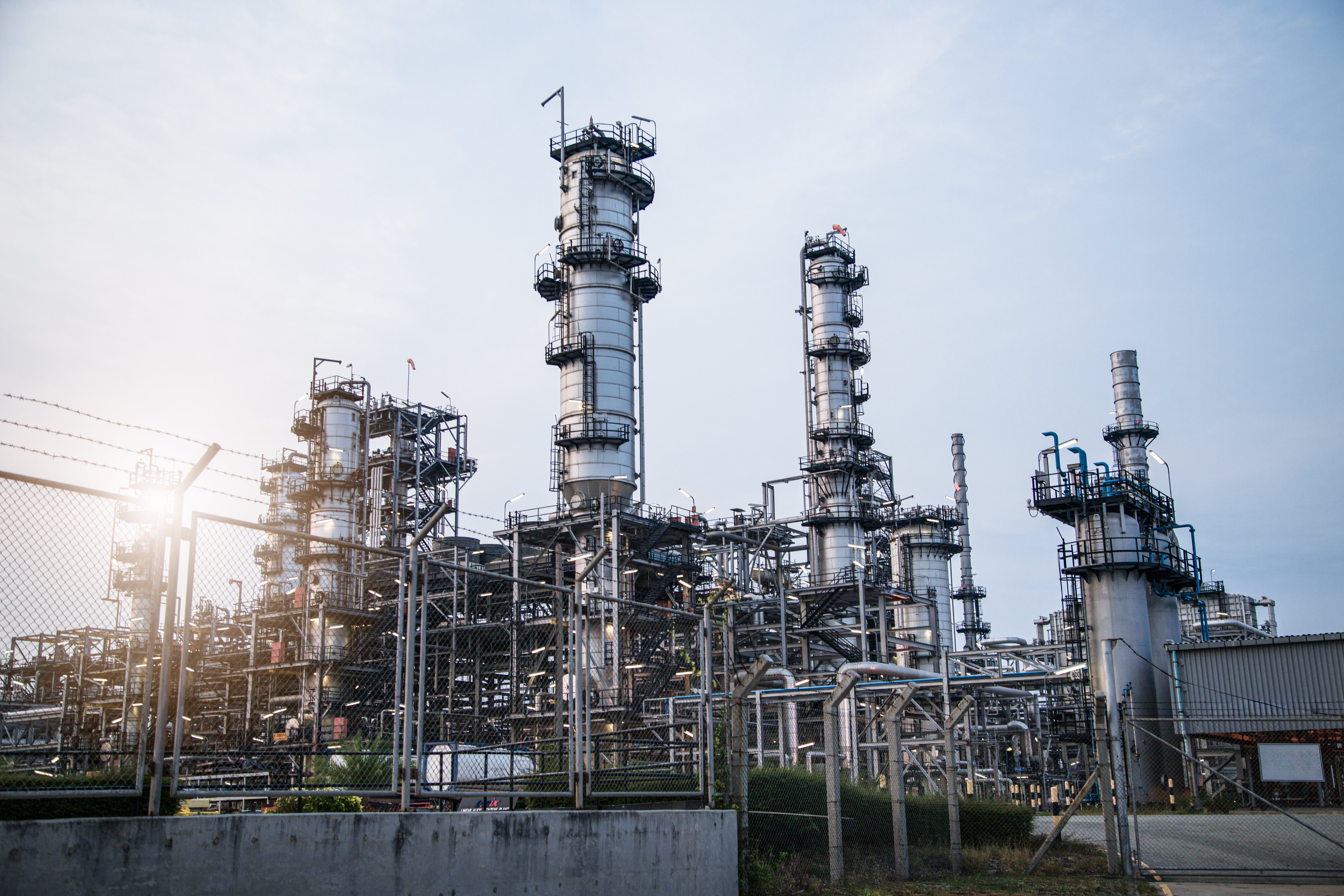 Industriell raffinaderi med höga destillationstorn och rörledningar mot blå himmel