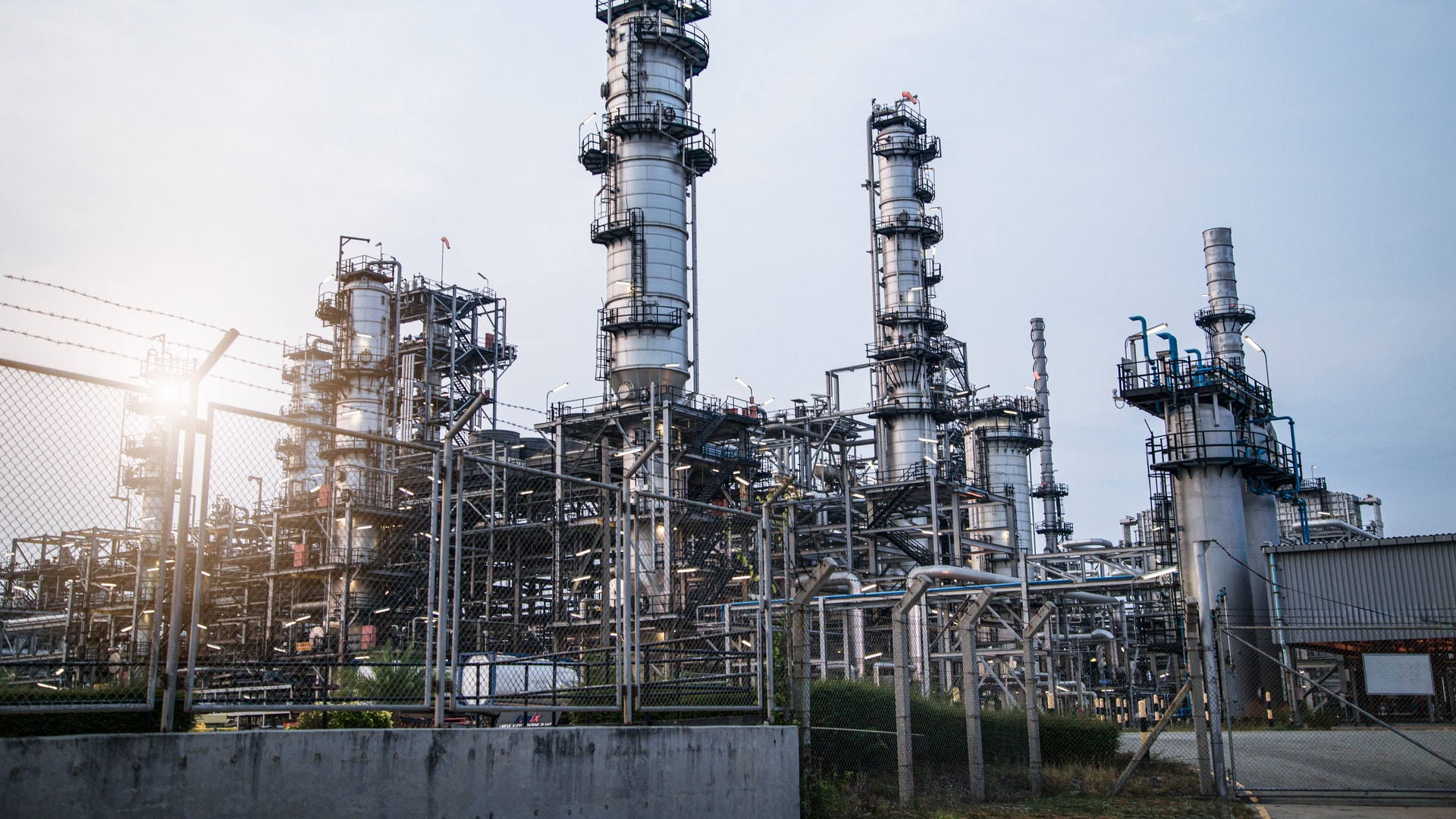 Industriell raffinaderi med höga destillationstorn och rörledningar mot blå himmel