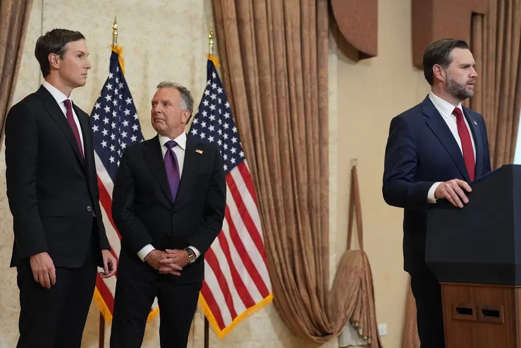 Tre män i formell affärsdräkt står i ett officiellt regeringsrum med amerikanska flaggor i bakgrunden.