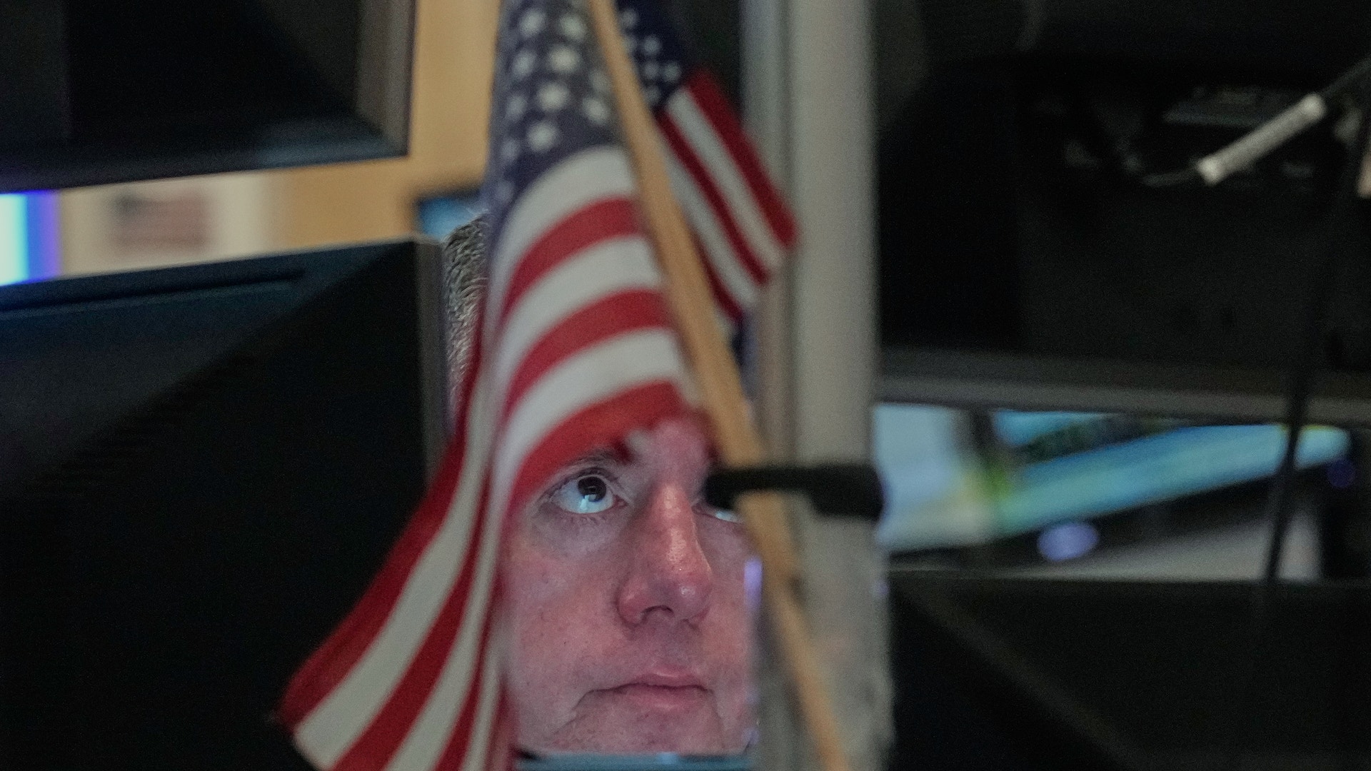 En person tittar upp medan en amerikansk flagga är placerad framför ansiktet. I bakgrunden syns datorskärmar.