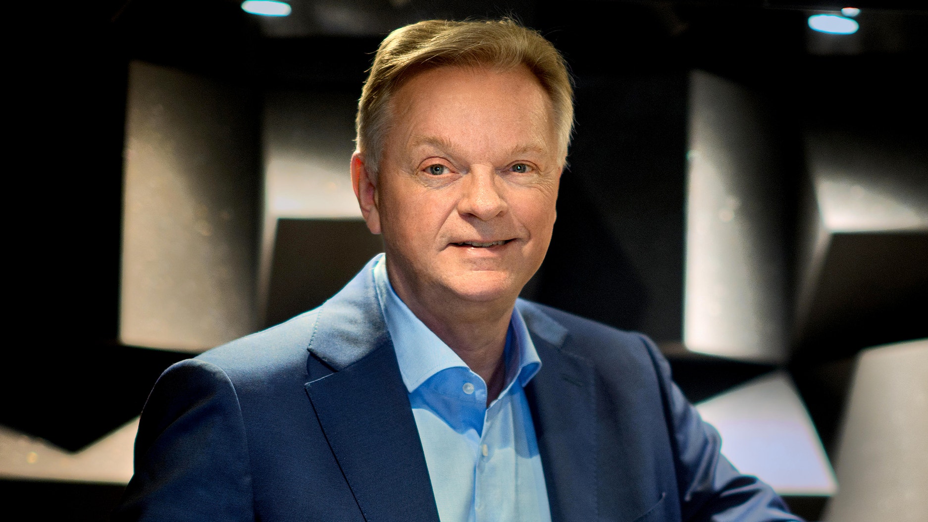 Porträttbild av en man i kostym som ler mot kameran i en tv-studio.