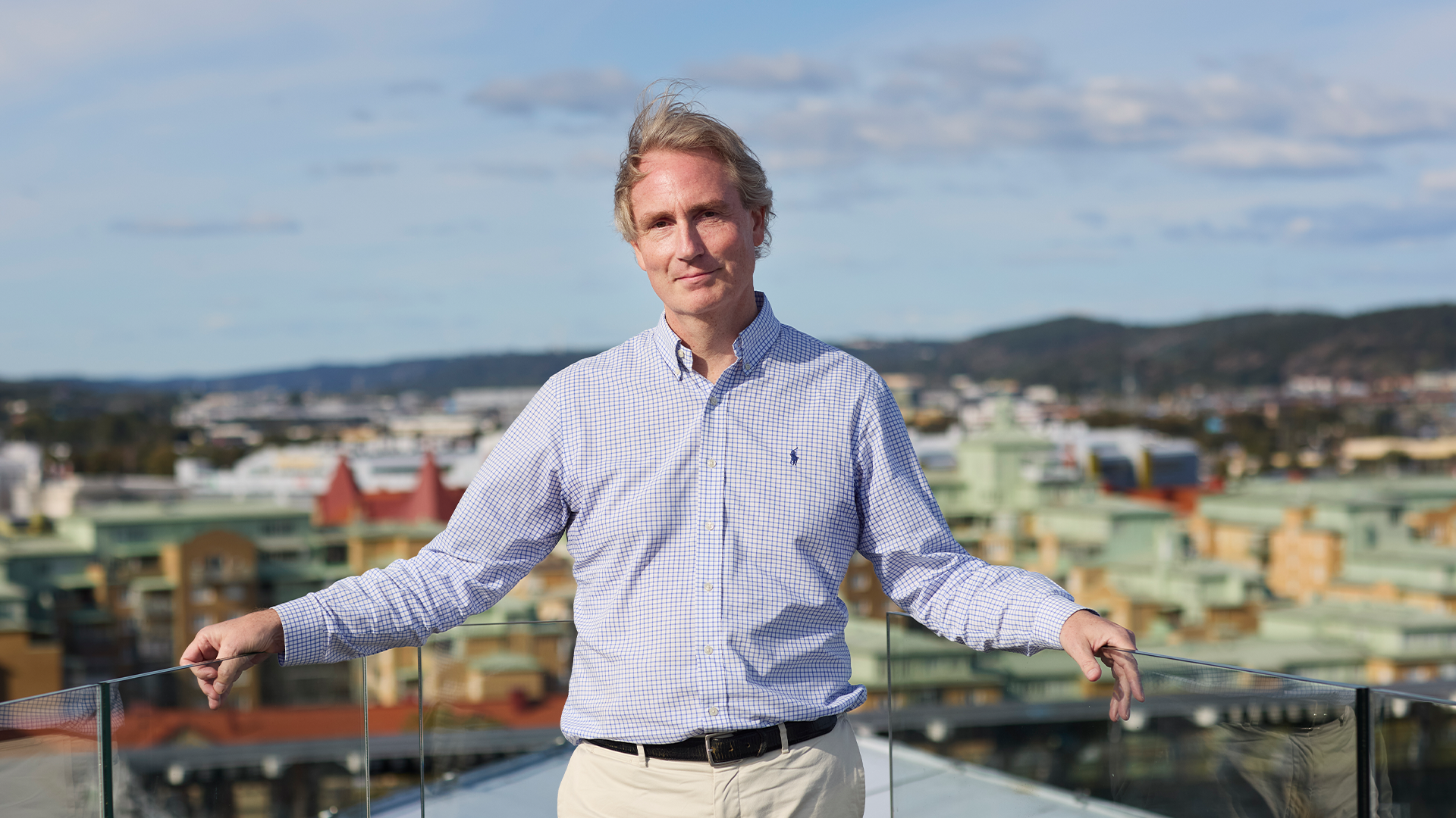 Erik Selin lutar sig mot staketet som omringar kontorets takterass. Bakom honom ser man Göteborgs skyline. Han ser glad ut och tittar in i kameran.
