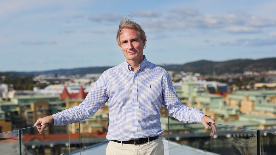Erik Selin lutar sig mot staketet som omringar kontorets takterass. Bakom honom ser man Göteborgs skyline. Han ser glad ut och tittar in i kameran.