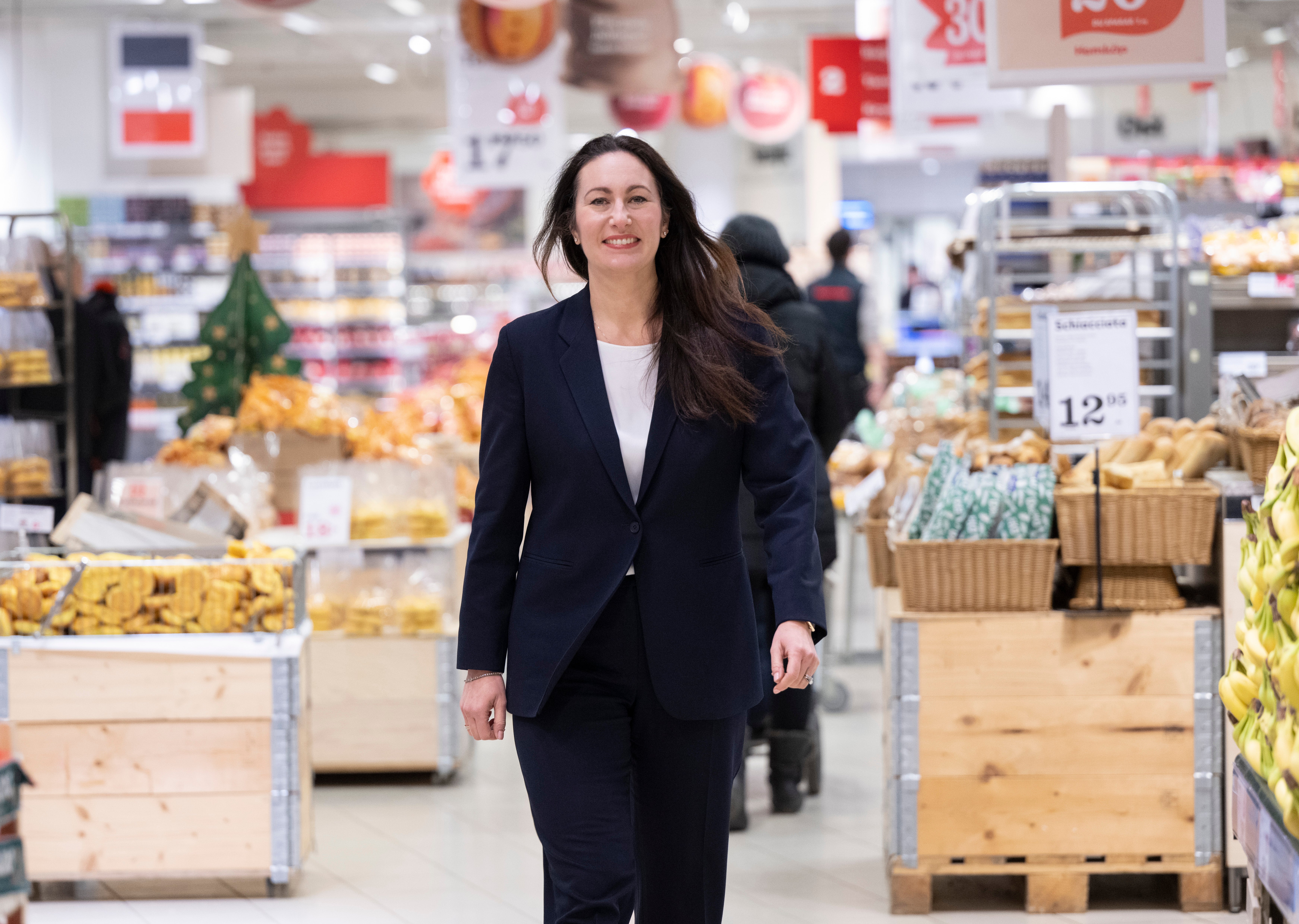 Kvinna i mörk kostym går genom en matbutik mellan hyllor med varor.