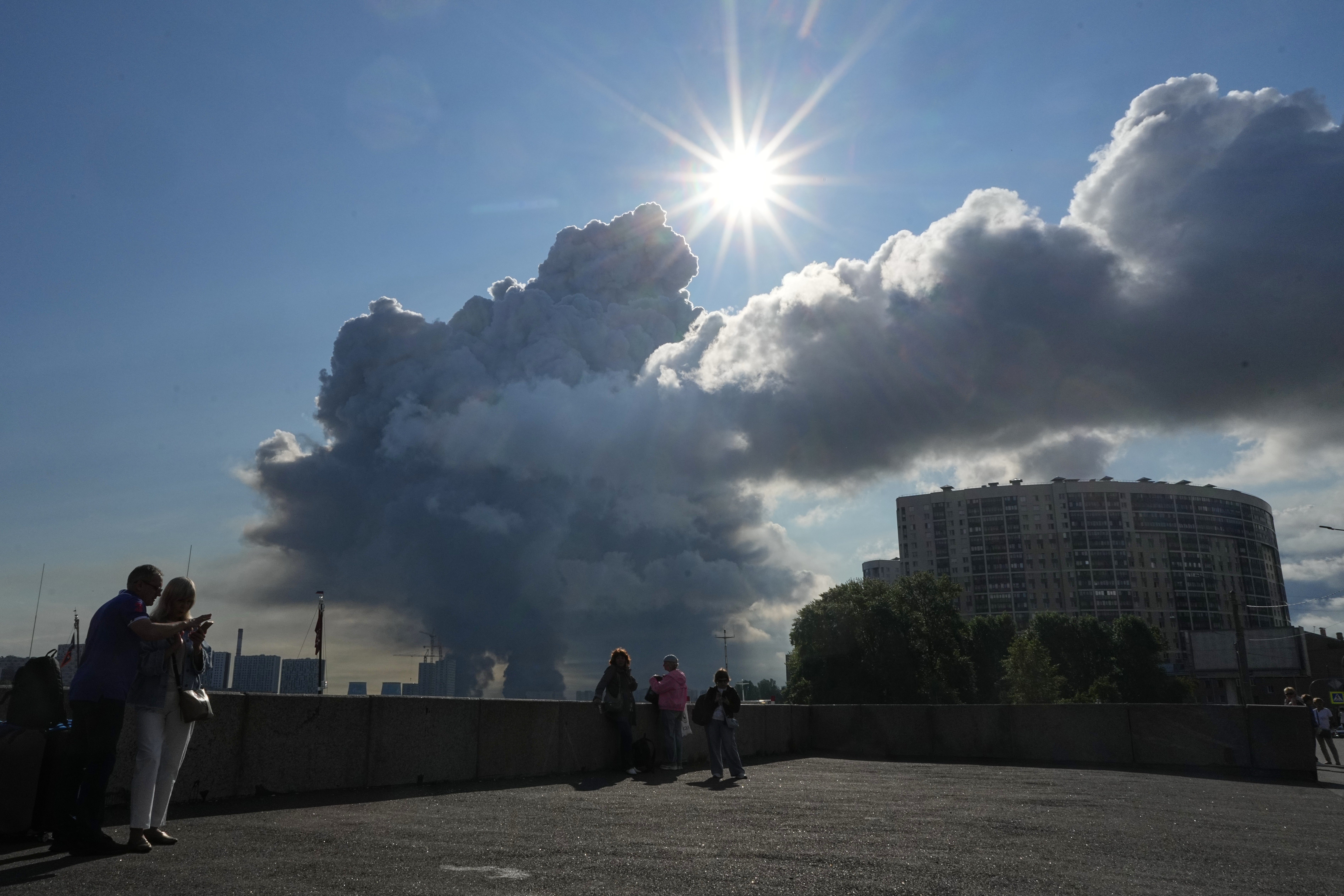 Människor står på en takterrass och tittar upp mot en dramatisk himmel med stora moln och starkt solljus. Moderna bostadshus syns i bakgrunden.