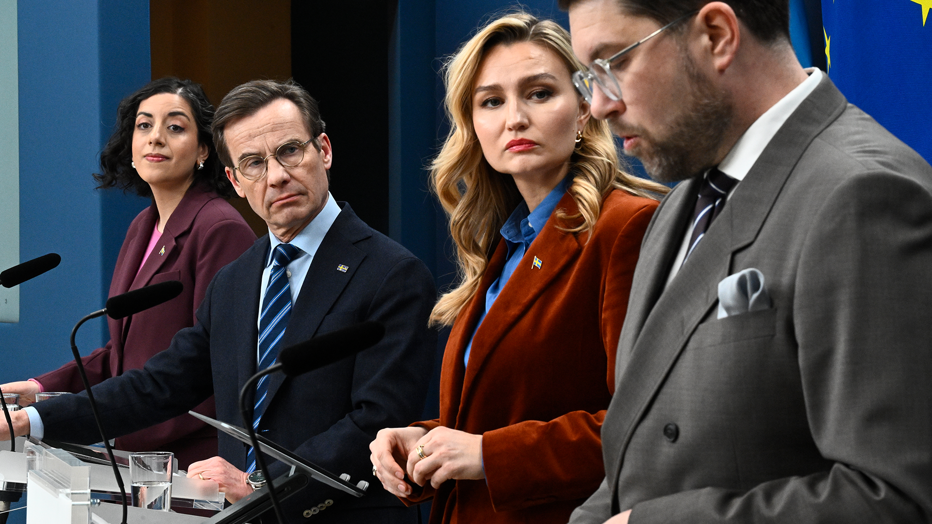Fyra personer i formell klädsel sitter vid ett bord med mikrofoner under en presskonferens eller officiell sammankomst.